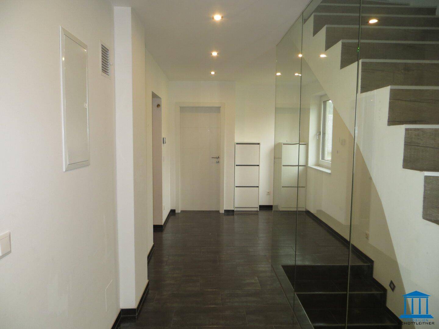 Heller Flur mit dunklem Fliesenboden und moderner Glas-Treppe.