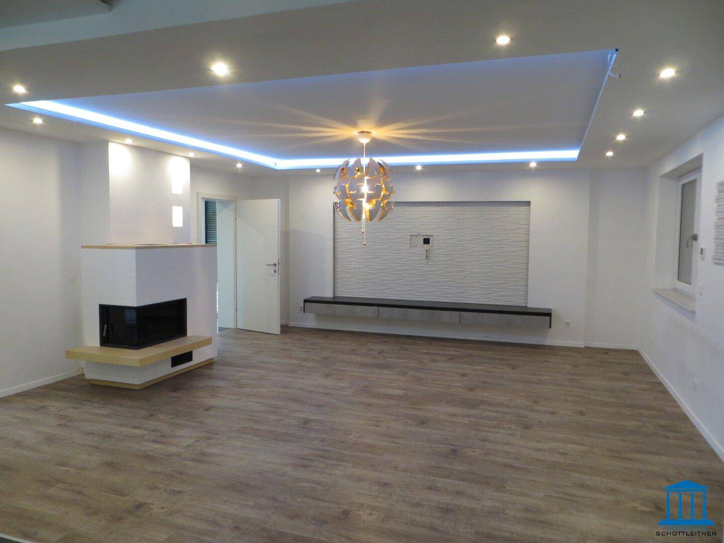 Geräumiges Wohnzimmer mit Kamin, indirekter Beleuchtung und großen Fenstern.