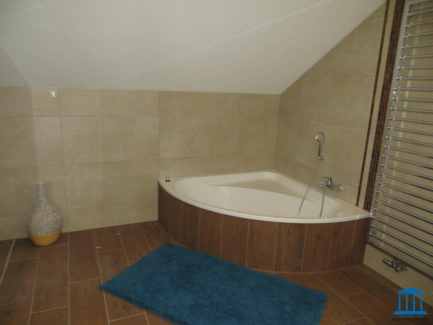 Badezimmer im Dachgeschoss mit Eckbadewanne, Fliesenboden und beheiztem Handtuchhalter.