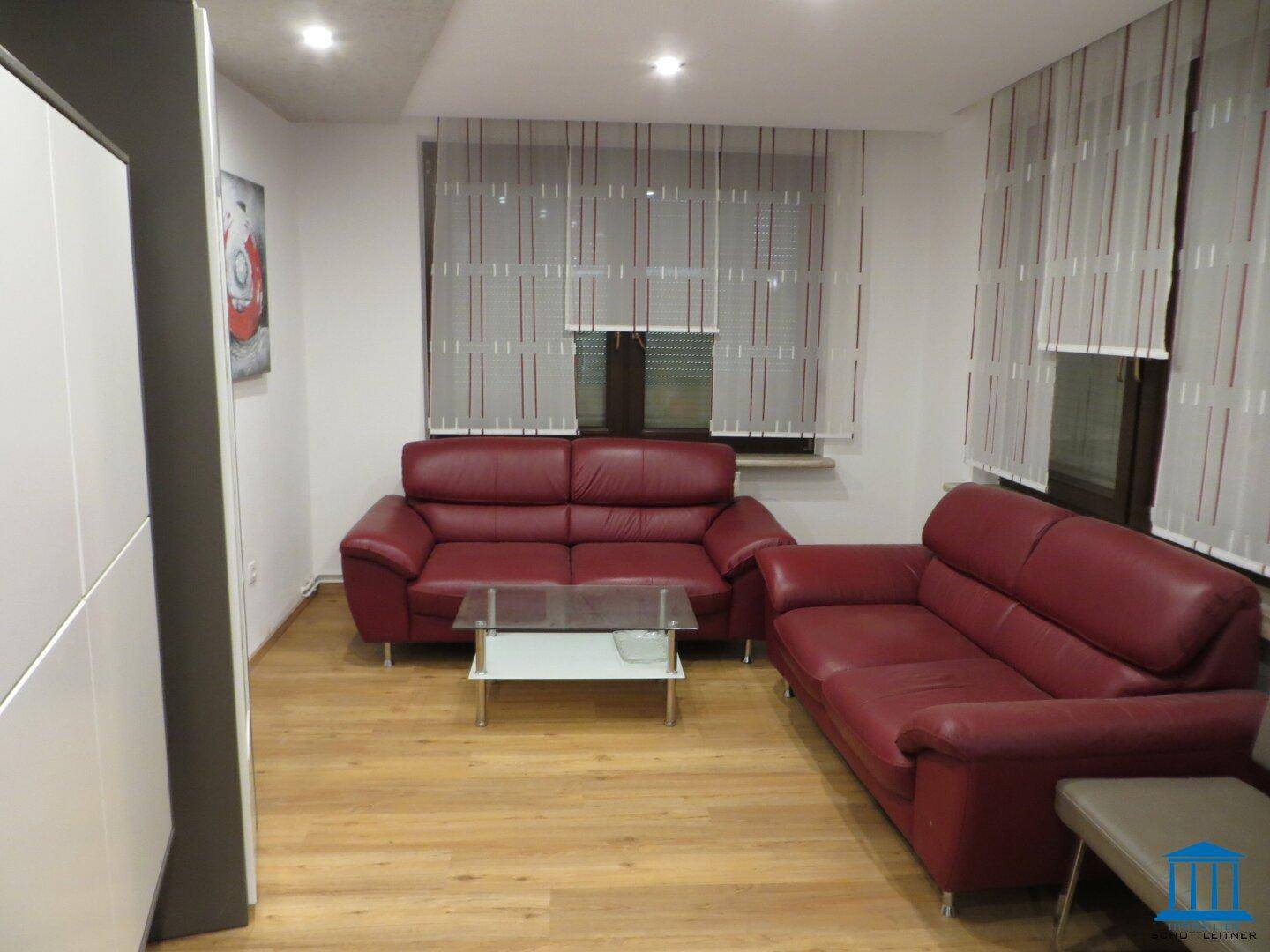 Wohnzimmer mit roten Ledersofas, Holzboden und großen Fenstern.