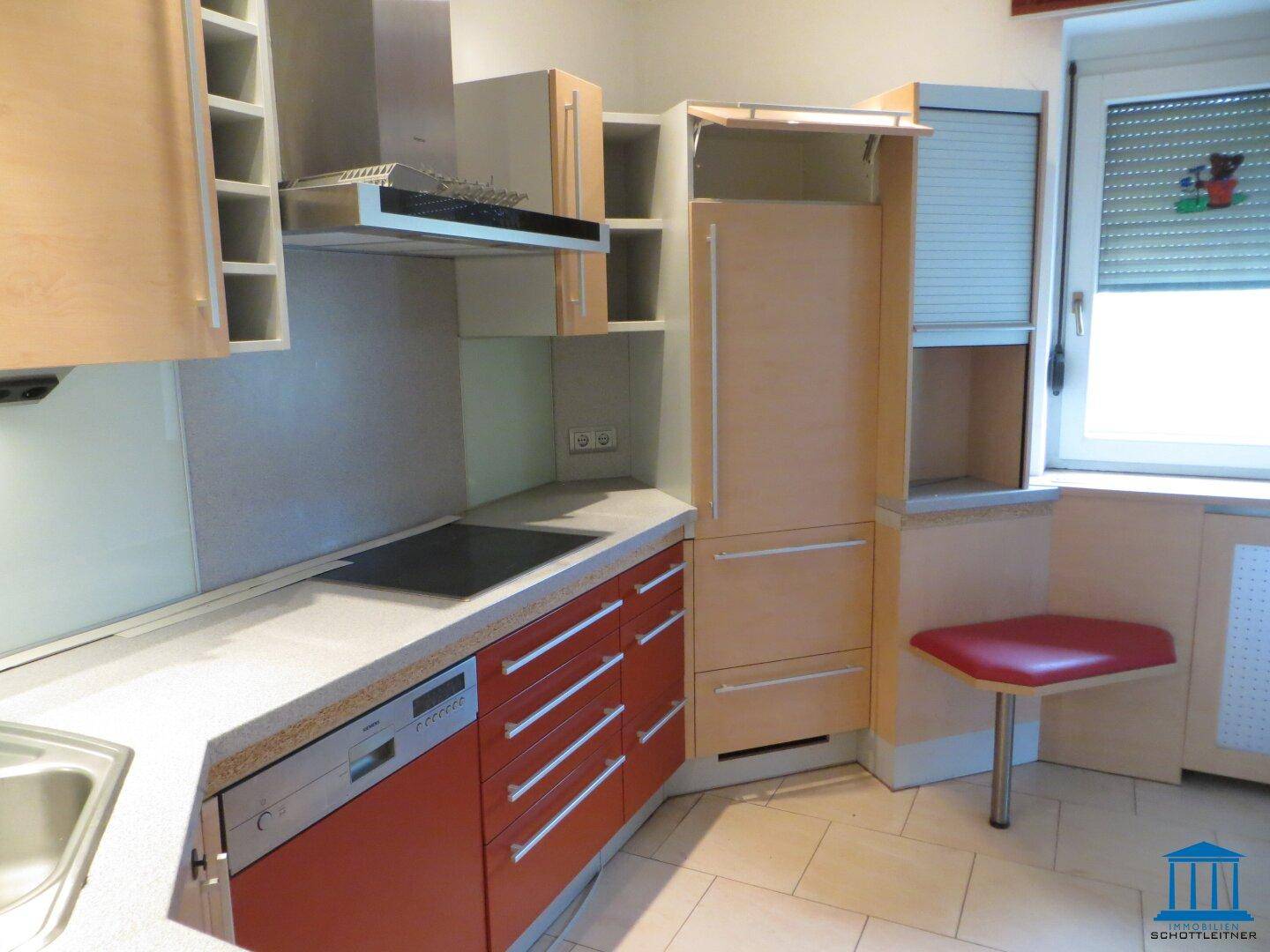 Küche mit roten und holzfarbenen Schränken, Einbaugeräten und Fliesenboden.