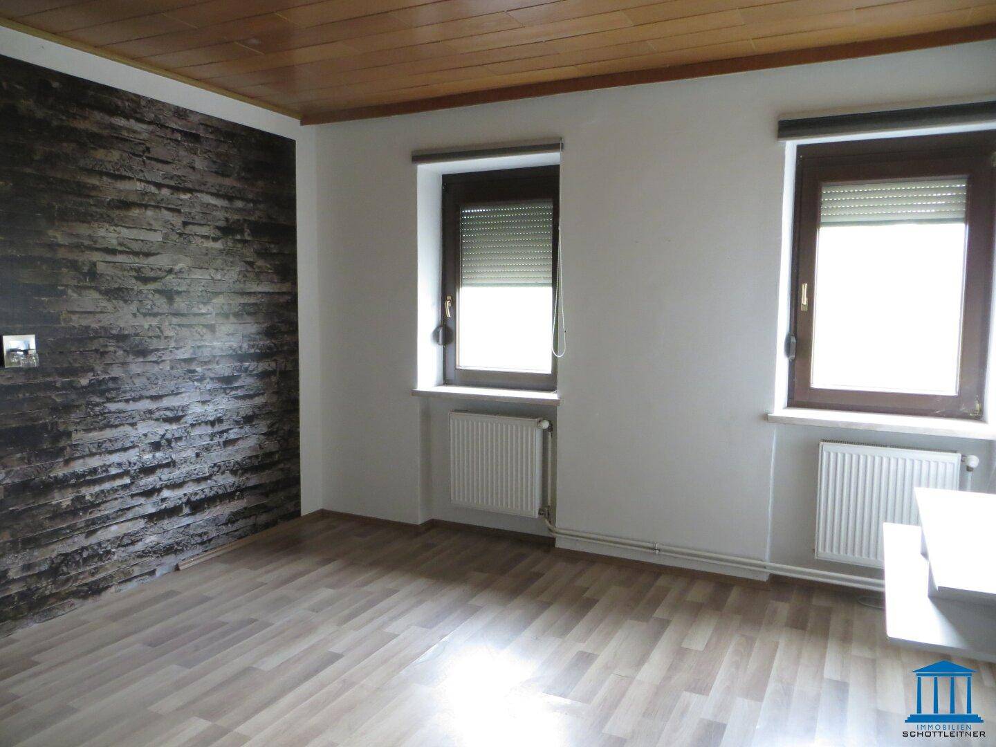 Raum mit Steinwand-Akzent, Holzboden und zwei Fenstern.