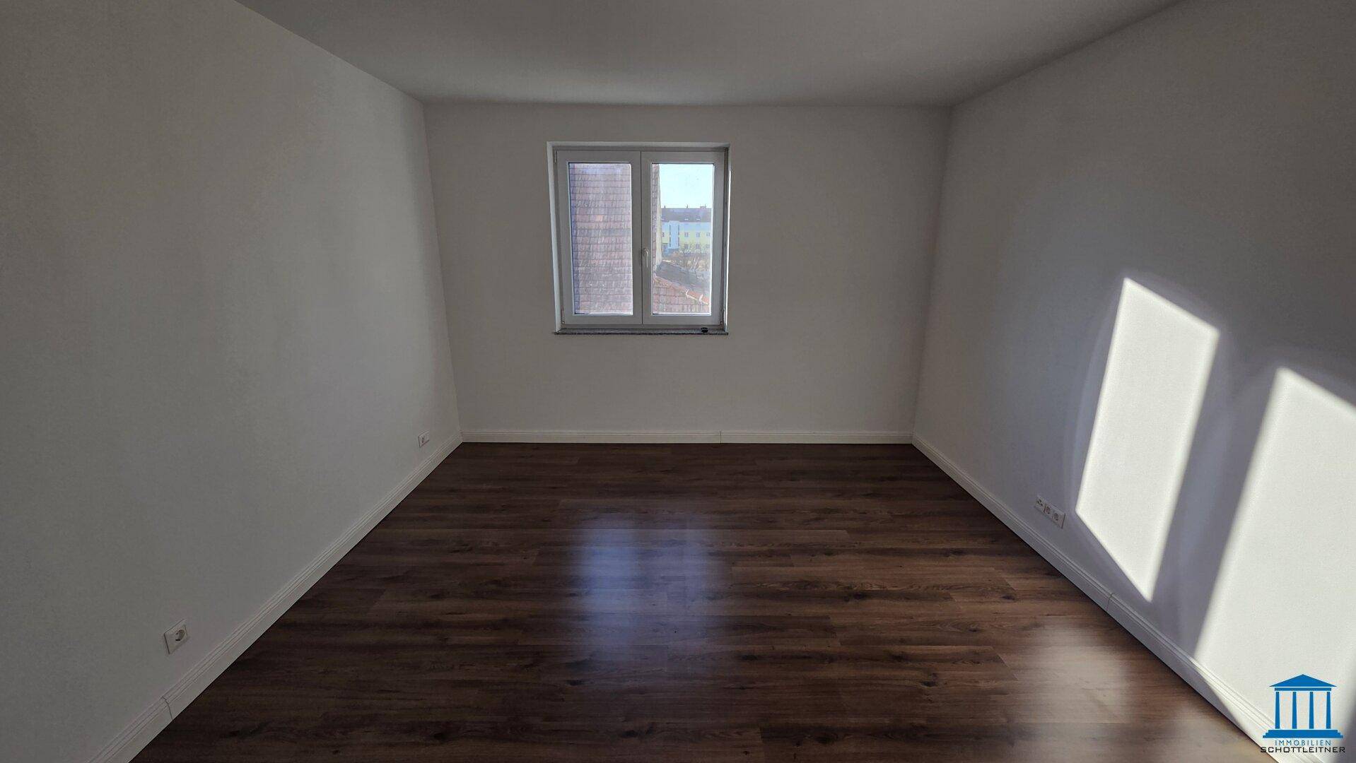 Geräumiges Schlafzimmer mit dunklem Laminatboden und einem Fenster, das viel Tageslicht spendet.