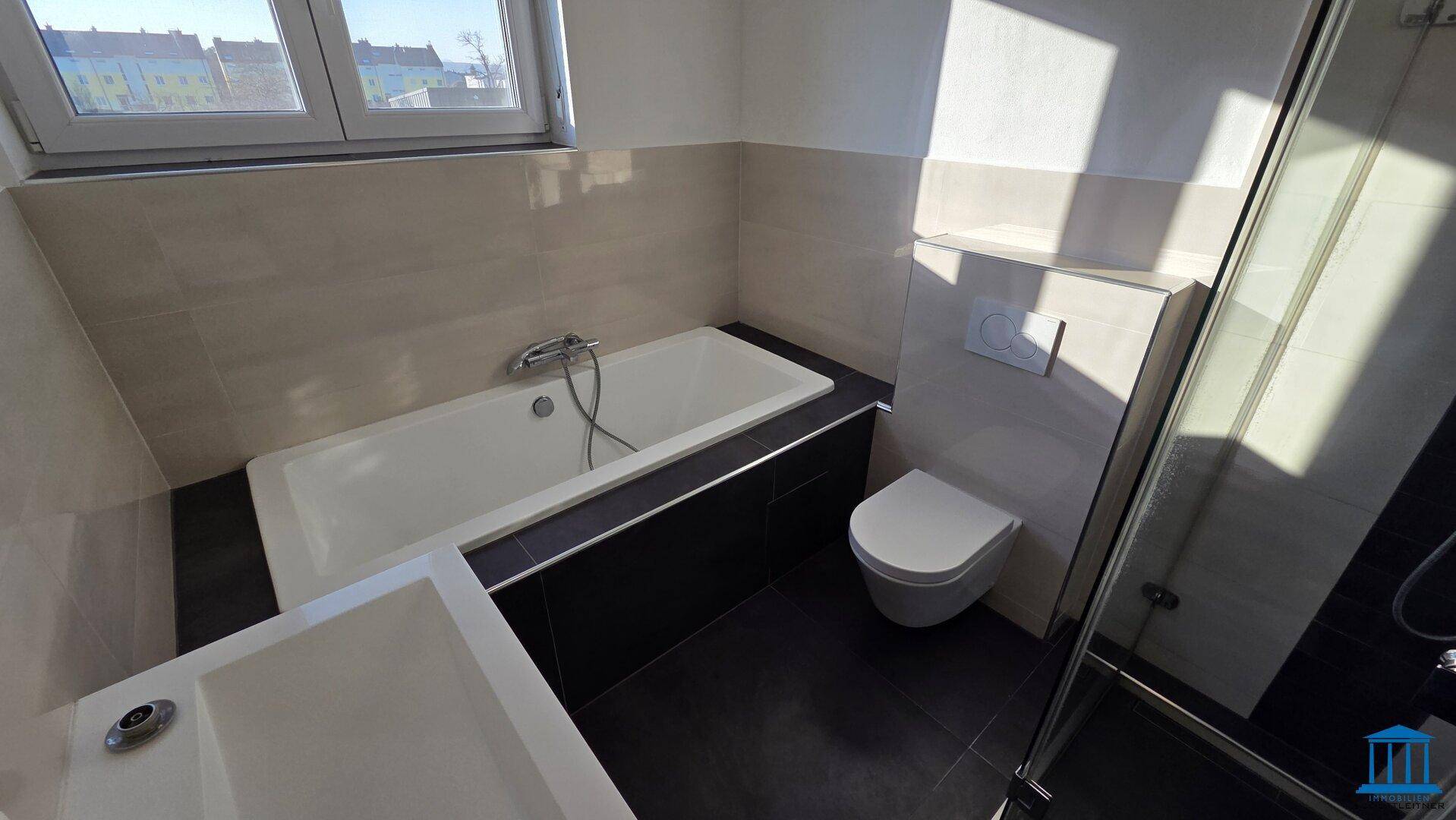 Helles Badezimmer mit Badewanne, wandhängendem WC und modernem Waschtisch mit Unterschrank.