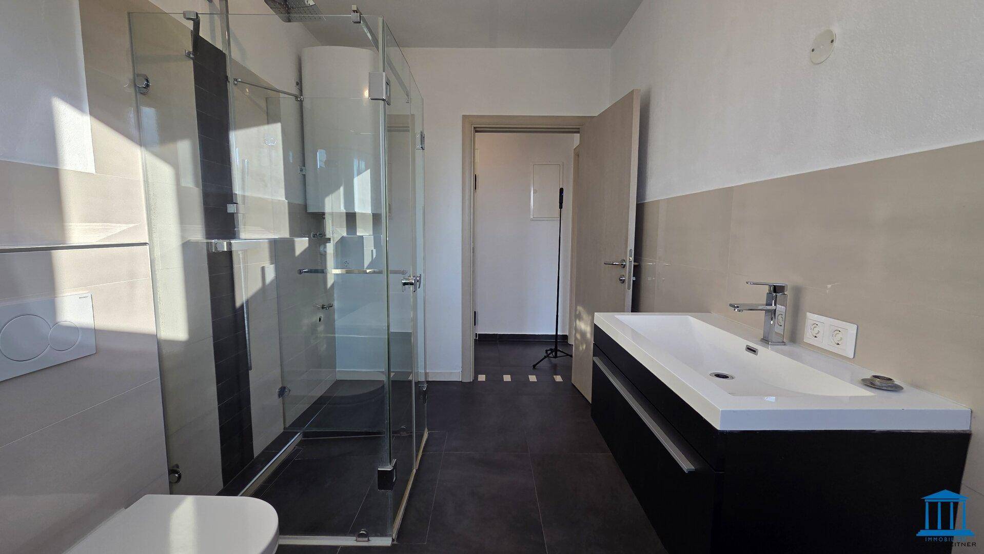 Modernes Badezimmer mit Glasdusche, wandhängendem WC und Waschtisch mit Unterschrank.