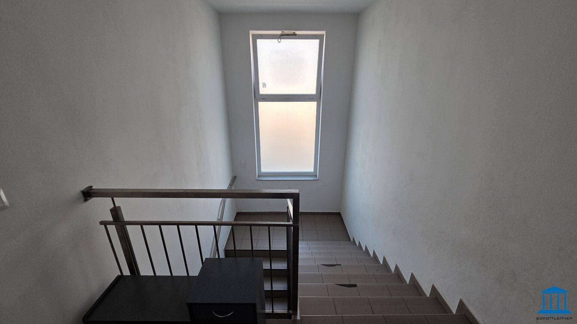 Treppenhaus mit Fliesenstufen, Metallgeländer und einem Fenster für natürliche Belichtung im Gebäude.