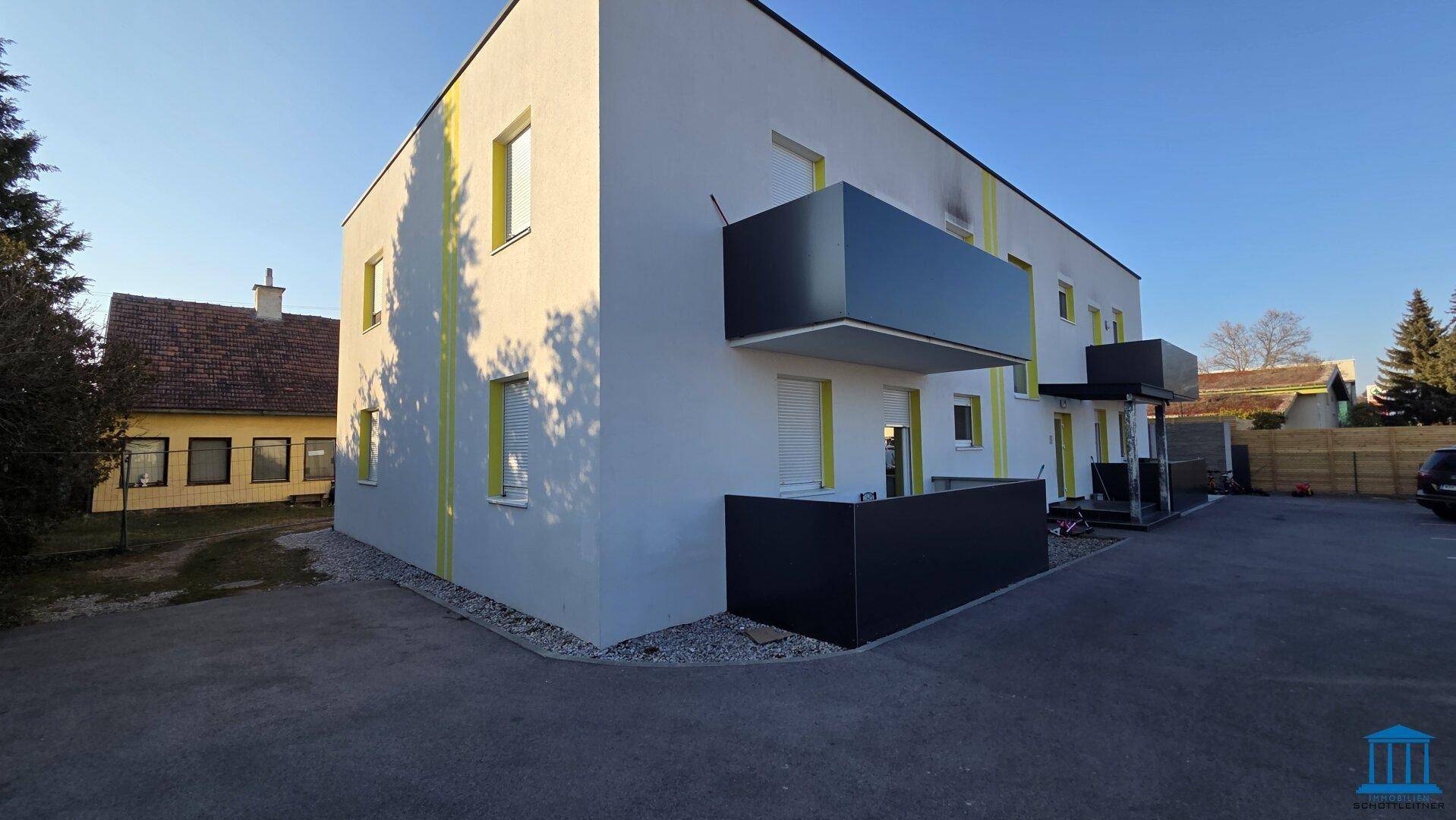 Modernes Mehrfamilienhaus mit gelben Akzenten, Balkonen und Außenparkplätzen unter blauem Himmel.