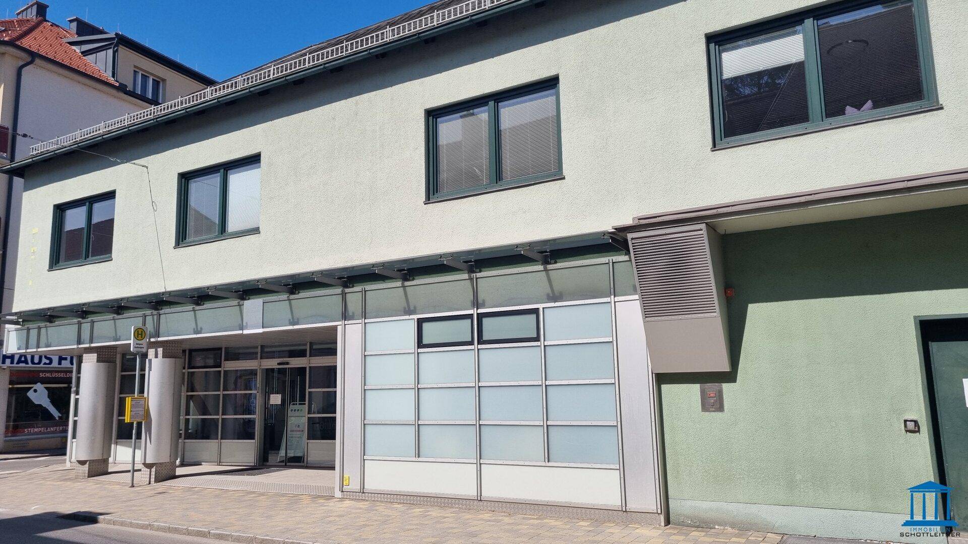Nahaufnahme der Gebäudefassade mit großen Fenstern und einem Eingangsbereich, der auf die Straße führt.