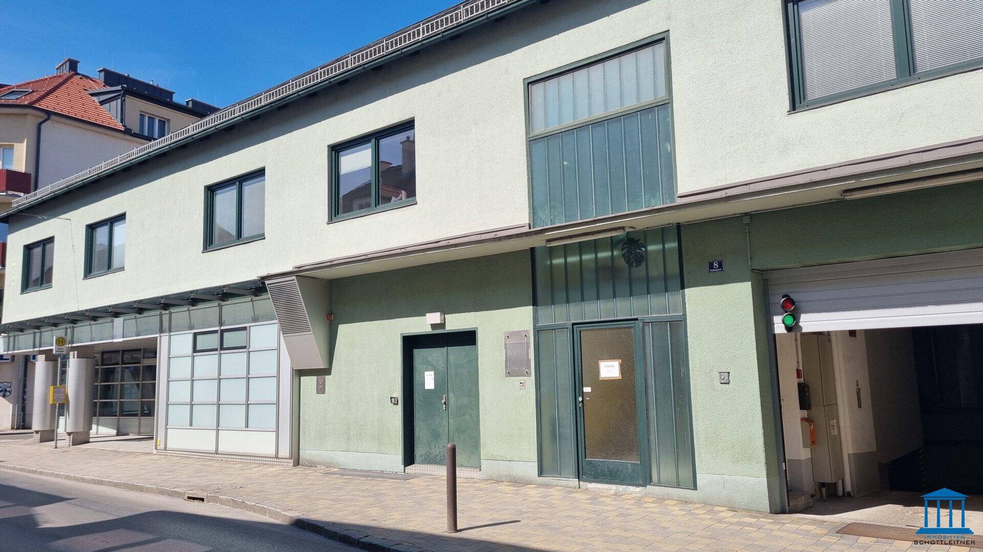 Seitenansicht der Gebäudefassade mit Garagentor und weiteren Fenstern, die auf die Straße blicken.