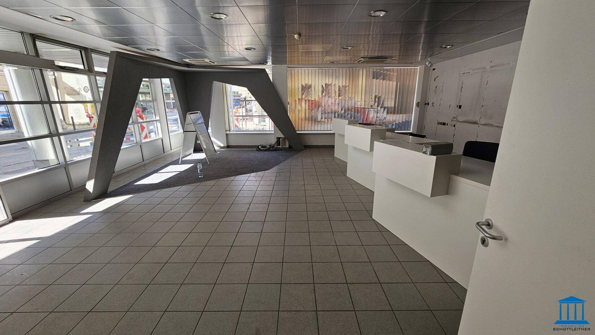 Geräumiger Büroraum mit Fliesenboden, großen Fenstern und modernen Empfangstheken.