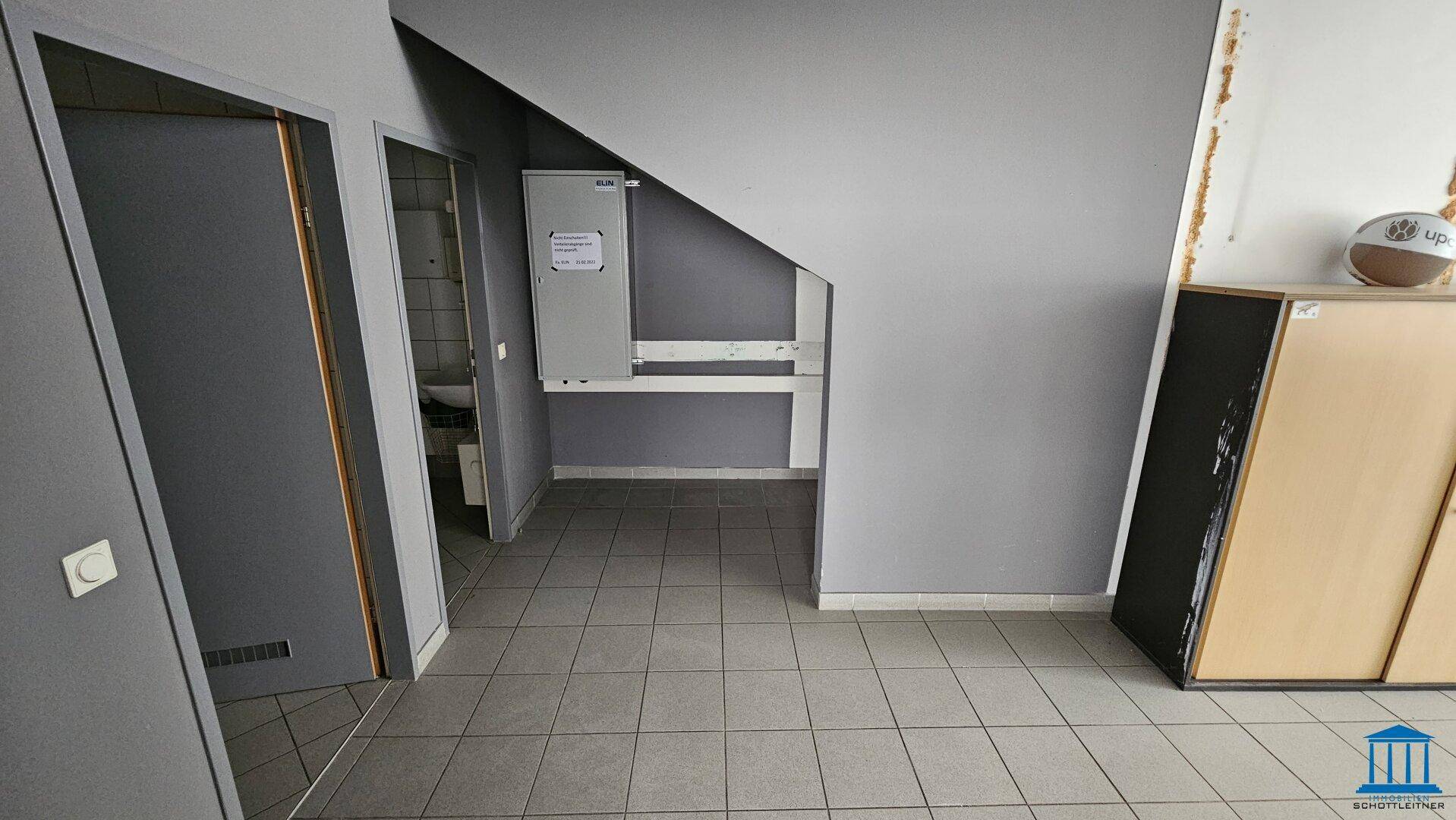 Flur mit Fliesenboden und Zugang zu den Toiletten, unter einer Treppe gelegen.