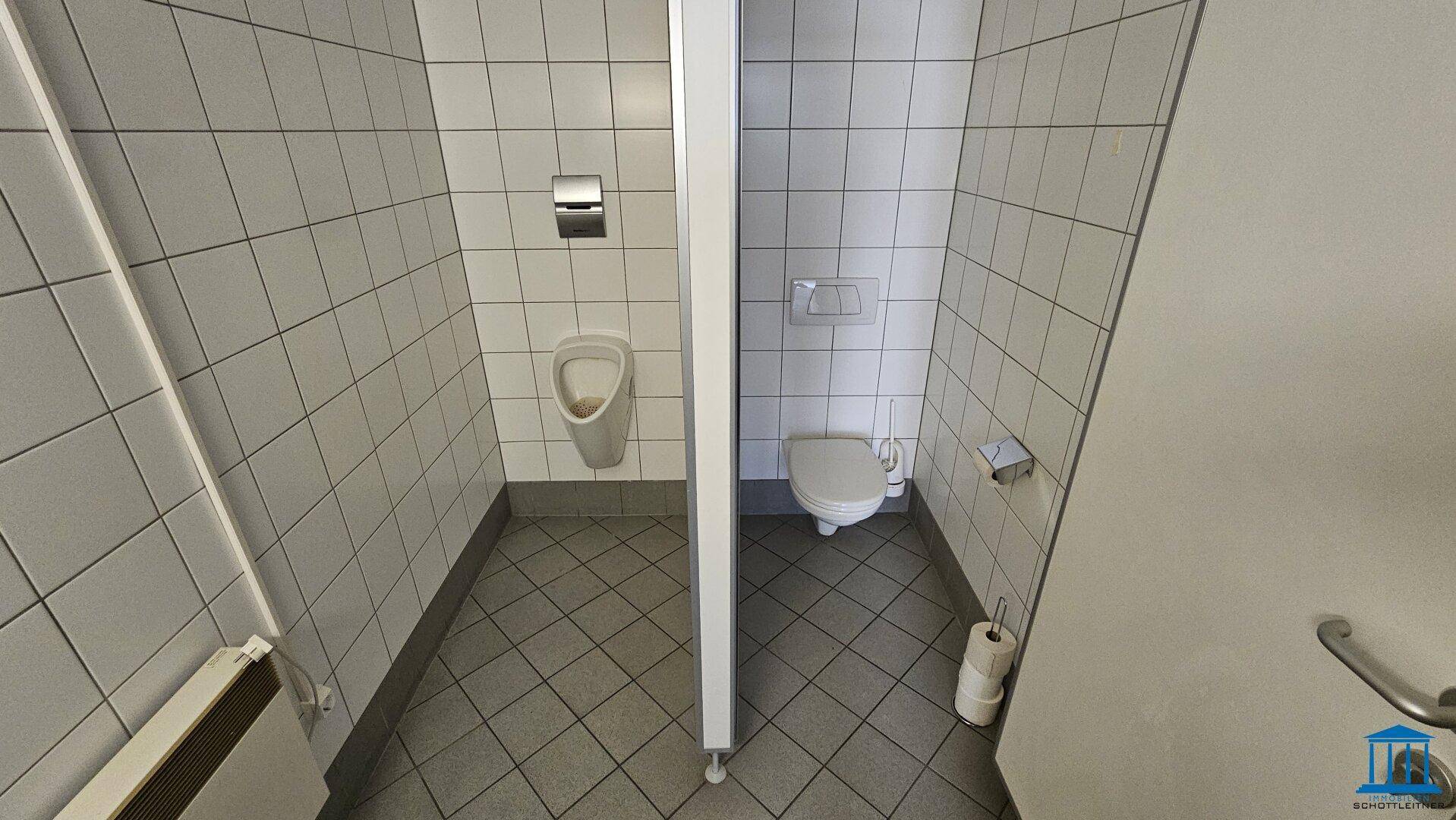 Toilettenraum mit Urinal und WC, ausgestattet mit weißen Fliesen und Heizung.