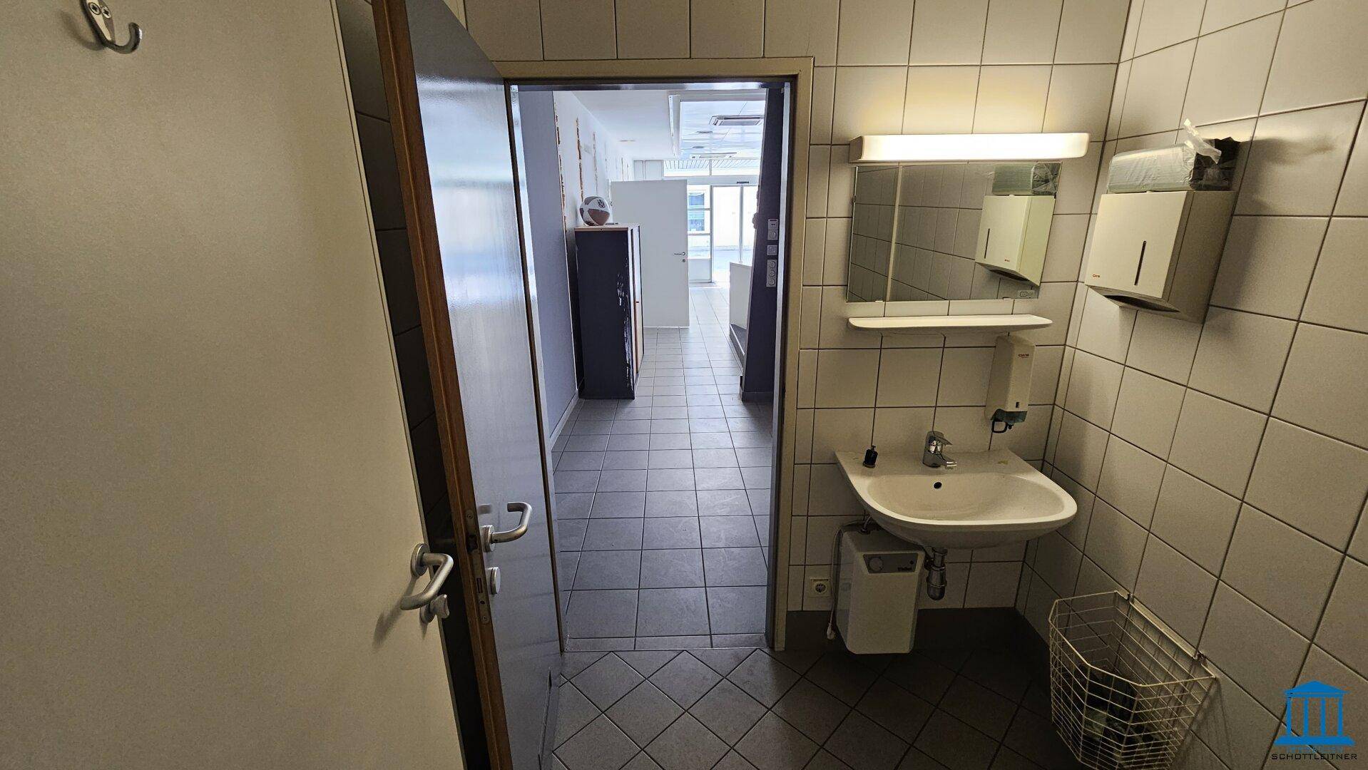 Waschbereich mit Waschbecken und Spiegel, der zu einem weiteren Raum führt.