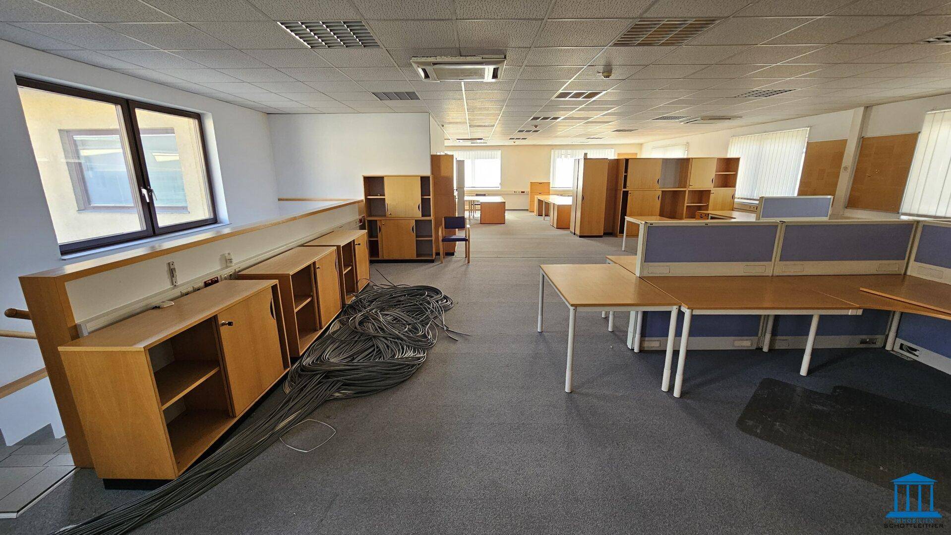 Großes Büro im Obergeschoss mit Teppichboden, Fenstern und Holzschränken.
