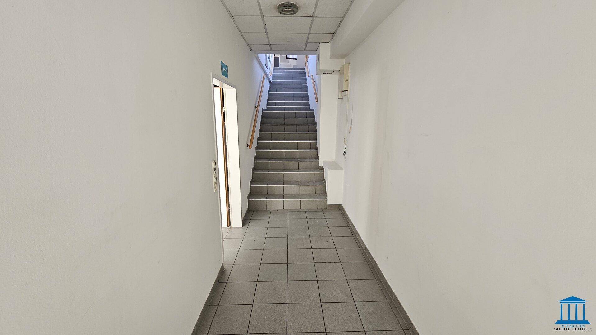 Langer Flur mit Fliesenboden und einer Treppe, die in die oberen Stockwerke führt.