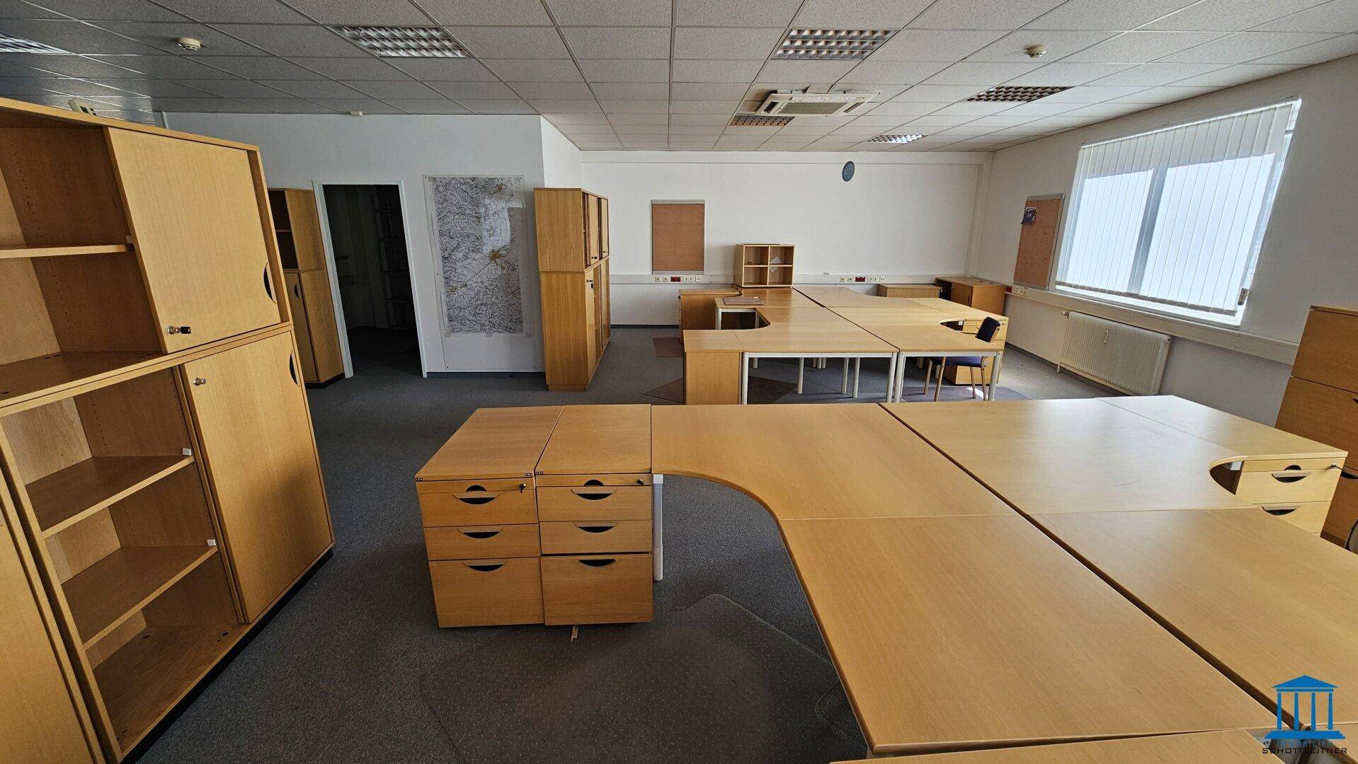 Großes Büro mit Teppichboden, vielen Schreibtischen und Schränken, bereit zur Nutzung.