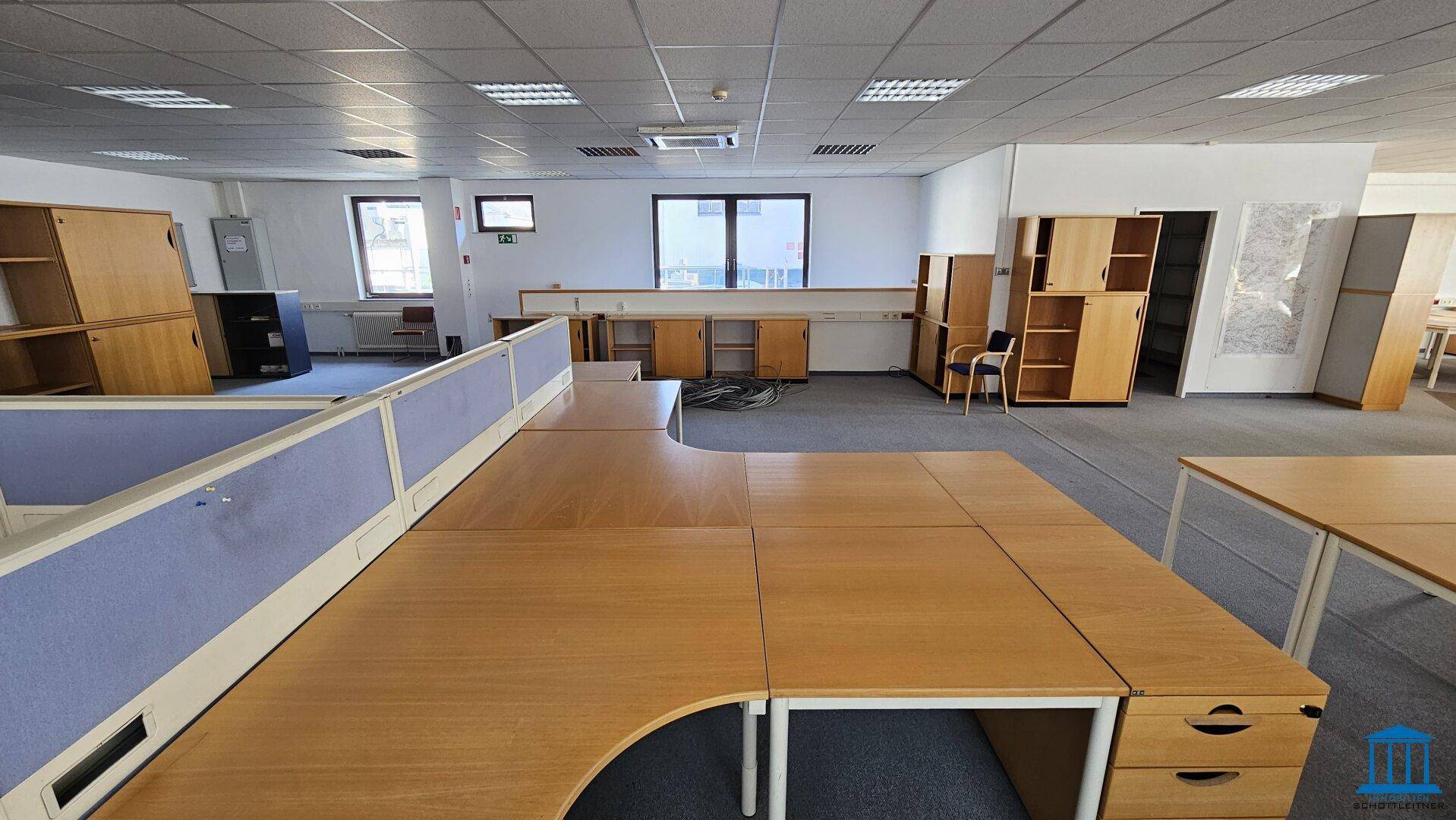 Modernes Büro mit Teppichboden, Schreibtischen und Trennwänden, die eine strukturierte Arbeitsumgebung schaffen.