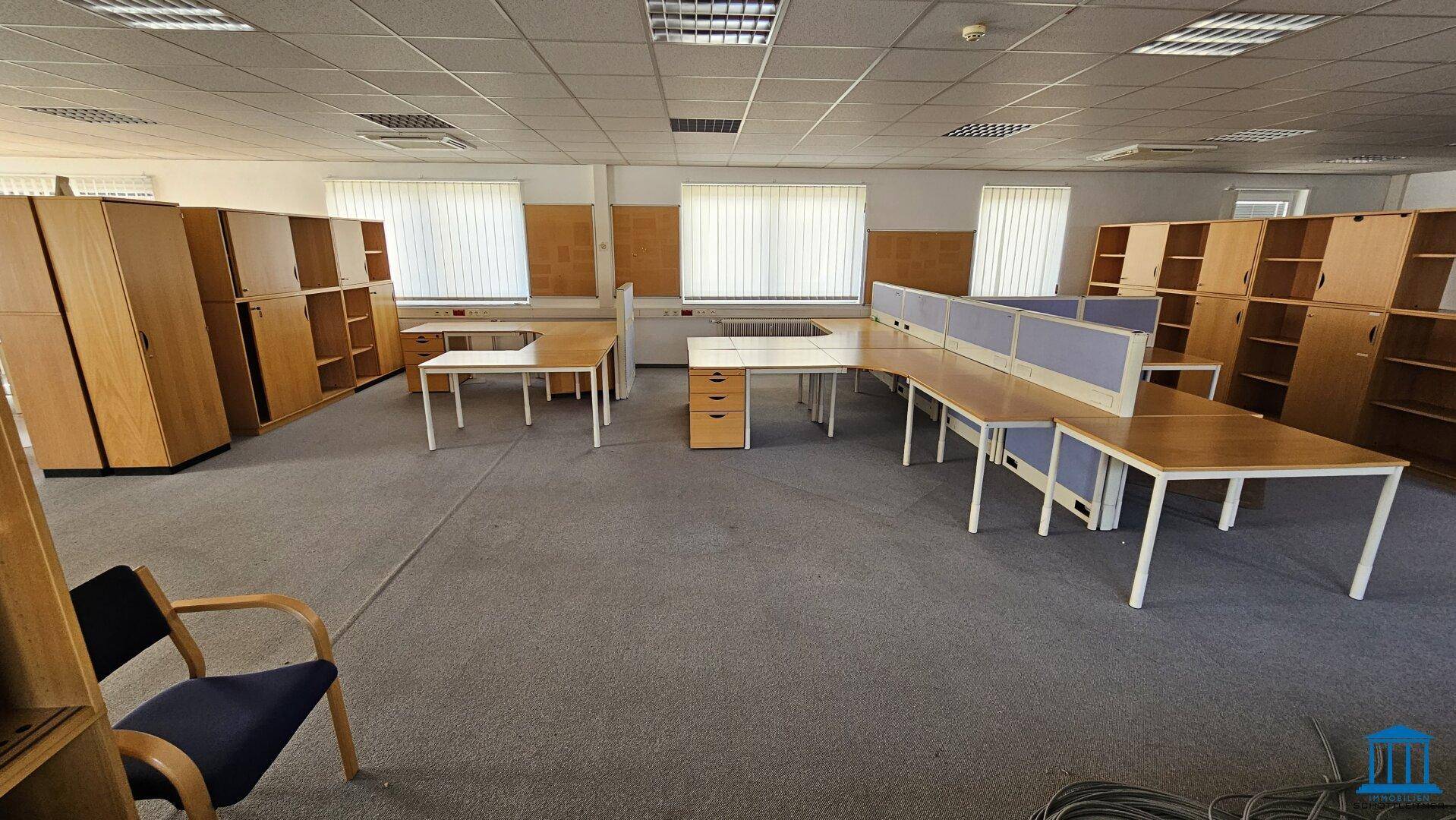 Großes Büro mit Teppichboden, vielen Schreibtischen und Schränken, ideal für ein großes Team.