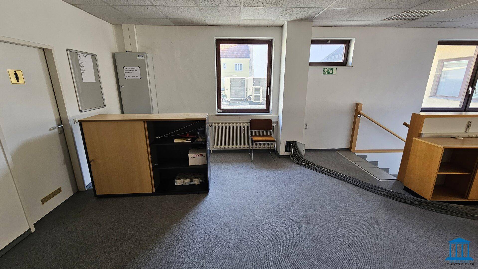 Geräumiger Bürobereich mit Teppichboden, Fenstern und einem Schrank, der viel Stauraum bietet.