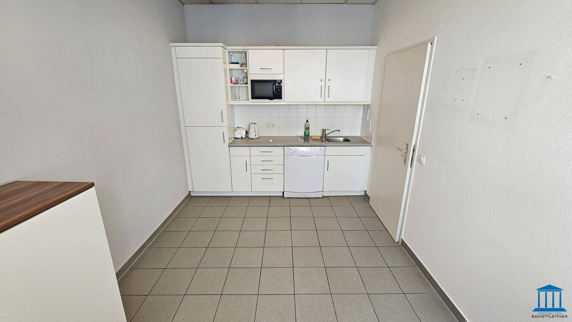 Kleine Einbauküche mit weißen Schränken, Spüle, Mikrowelle und Geschirrspüler in einem gefliesten Raum.