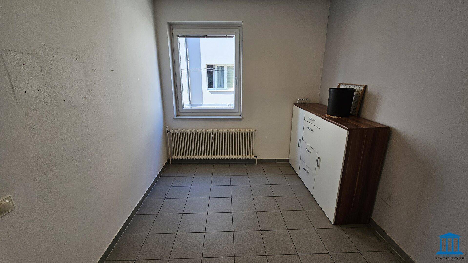 Leerer Büroraum mit Fliesenboden, einem Fenster und einem Sideboard, bereit zur Einrichtung.