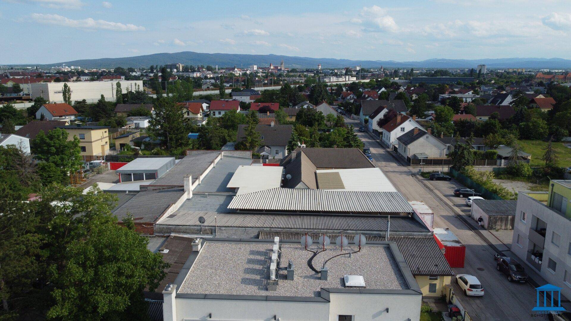 Blick von oben auf die Dächer des Gewerbekomplexes und die umliegende Stadtlandschaft mit vielen Gebäuden.