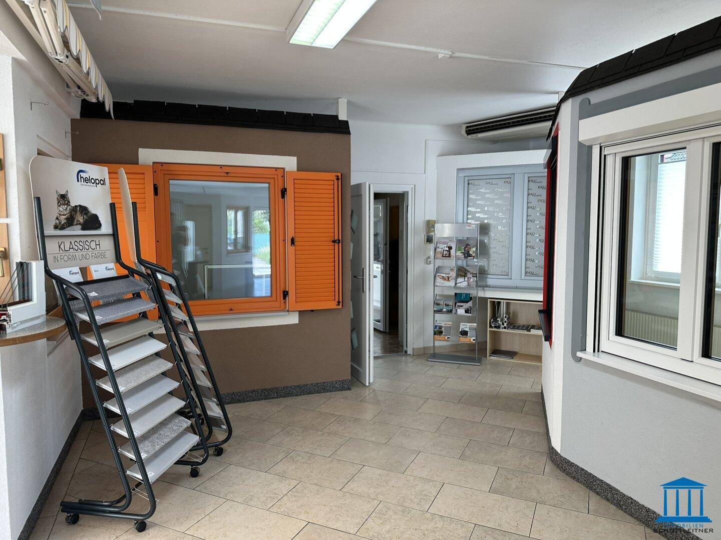 Ausstellungsfläche mit verschiedenen Fenster- und Türlösungen, darunter auch farbige Fensterläden, auf Fliesenboden.