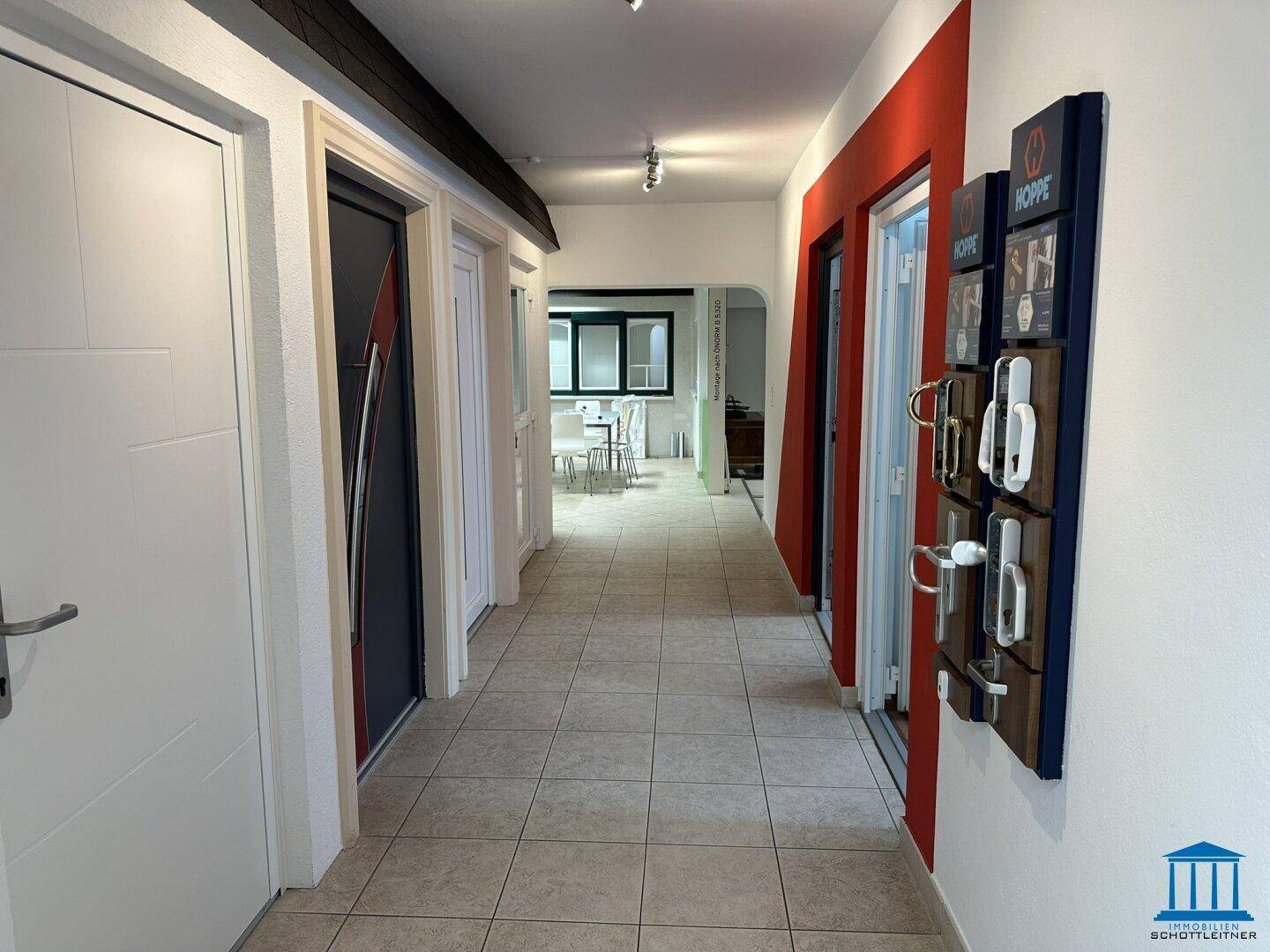 Langer Flur mit verschiedenen Türmodellen und Türgriffen als Ausstellungsstücke, führt zu weiteren Räumen.