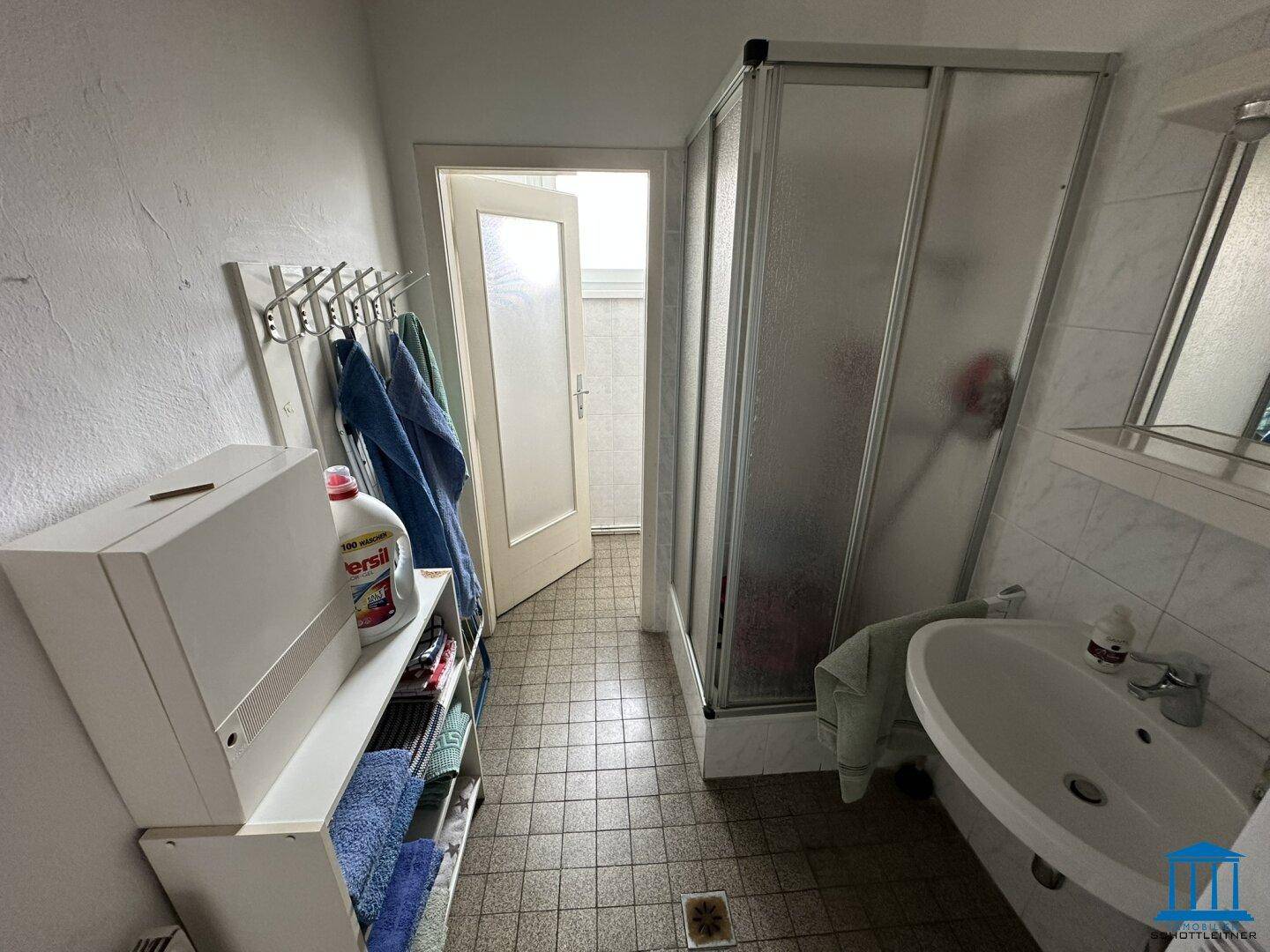 Kleines Badezimmer mit Duschkabine, Waschbecken und Fliesenboden, funktional eingerichtet.