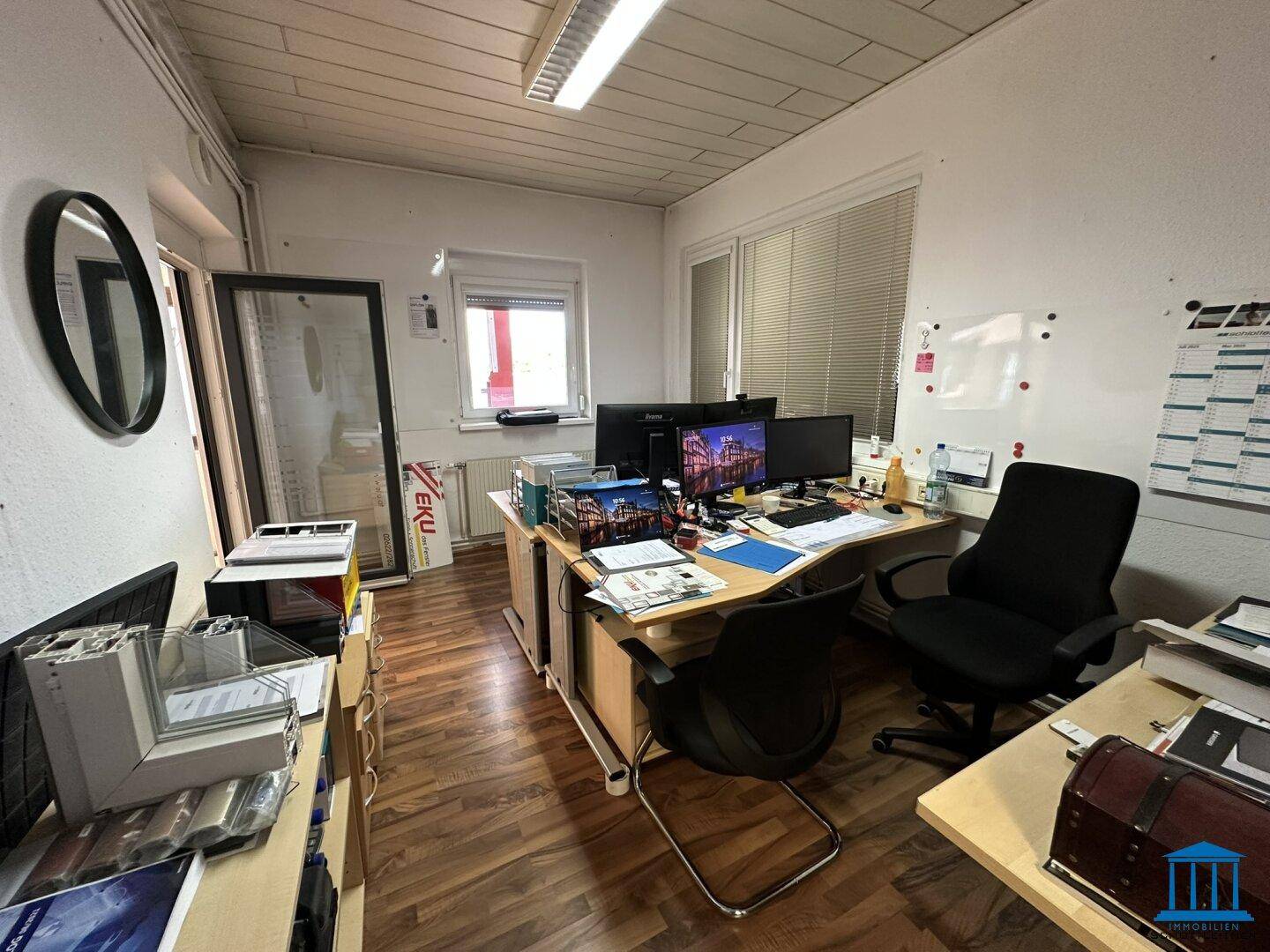 Büroarbeitsplatz mit Schreibtisch, Computern und einem Fenster, das Tageslicht hereinlässt.