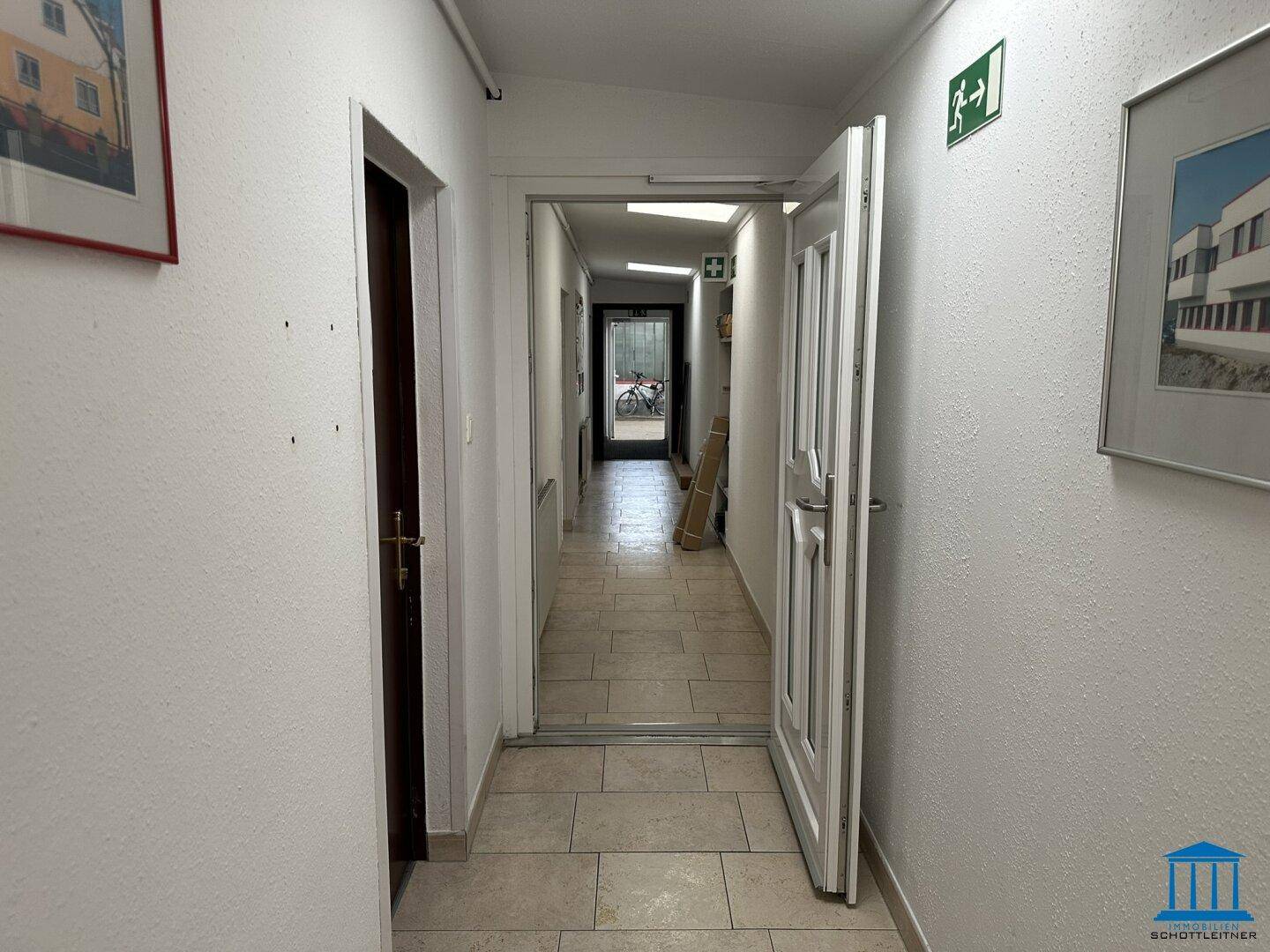 Heller Flur mit Fliesenboden, der zu weiteren Räumen führt, mit Notausgangsschildern.