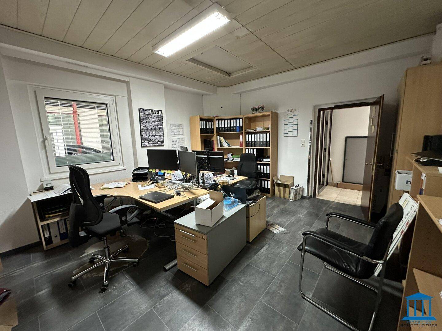 Geräumiges Büro mit mehreren Arbeitsplätzen, Regalen und einem dunklen Fliesenboden.