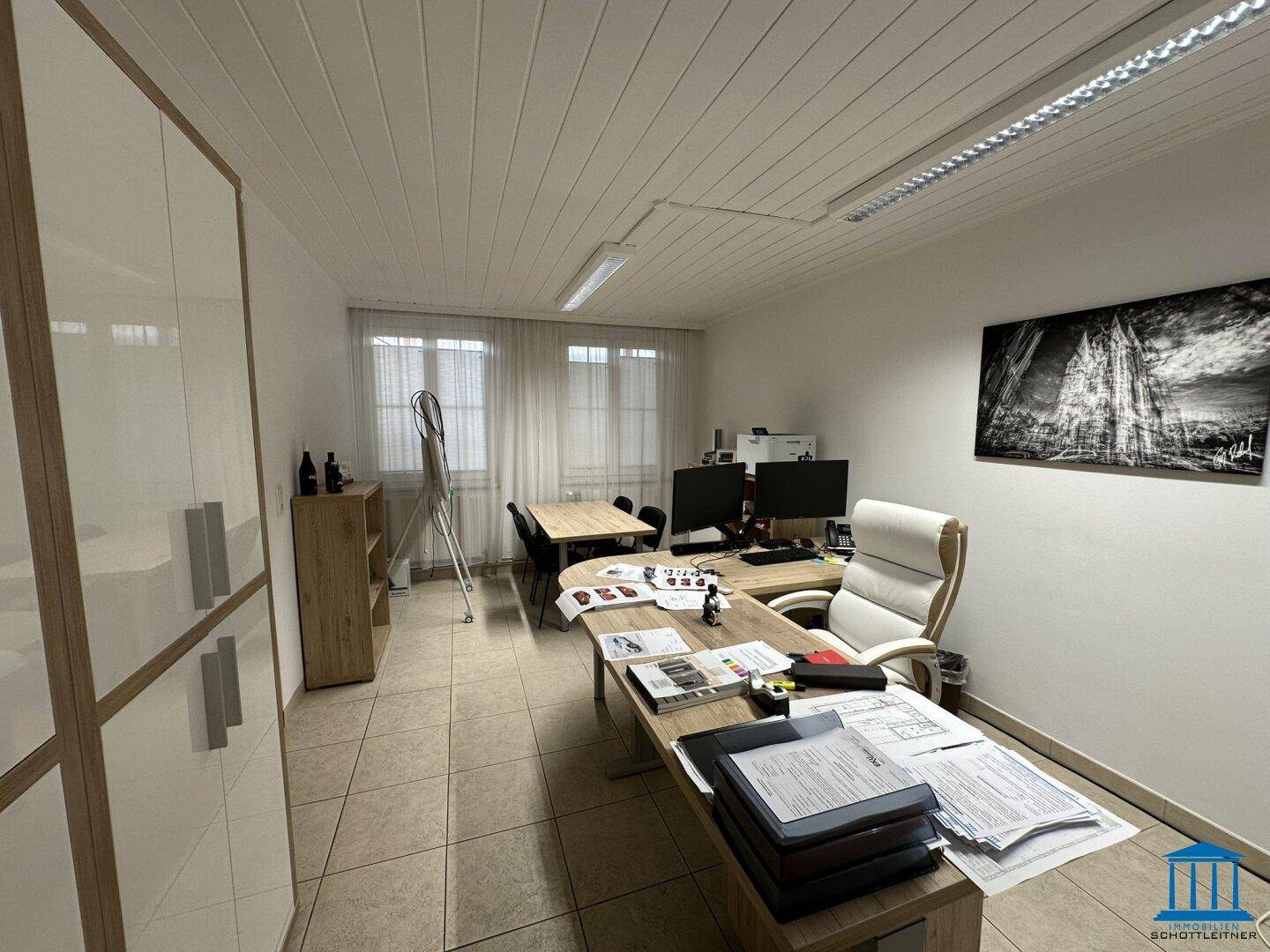 Geräumiges Büro mit mehreren Schreibtischen, Bürostühlen und einem großen Aktenschrank, gut beleuchtet.