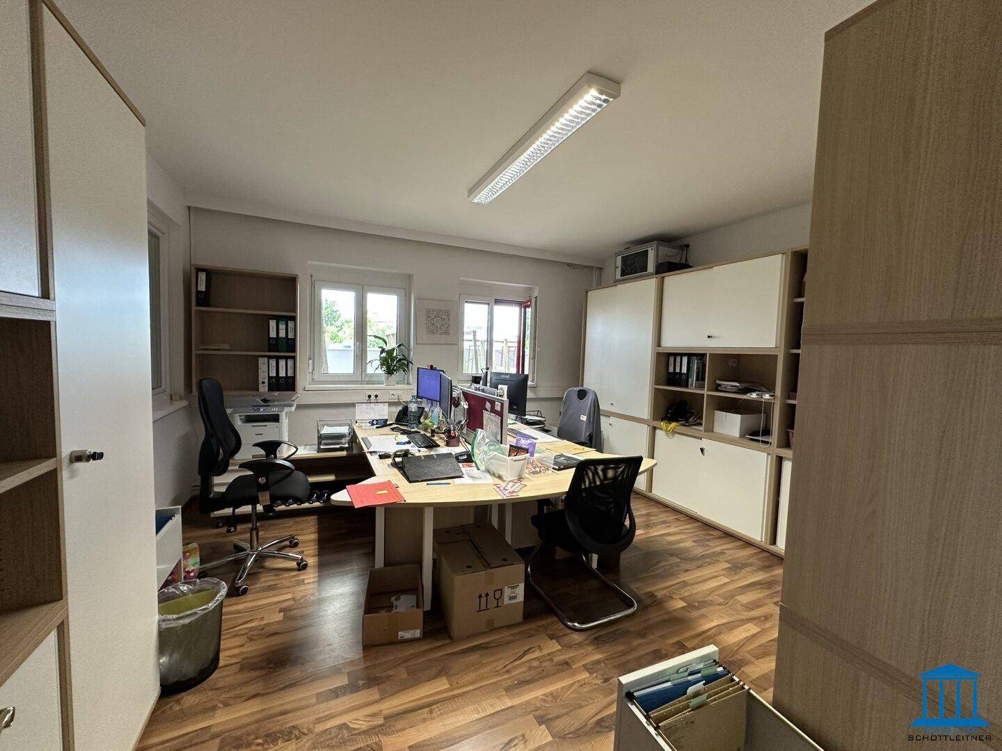 Großes Büro mit mehreren Arbeitsplätzen, Regalen voller Aktenordner und Holzoptik-Boden.