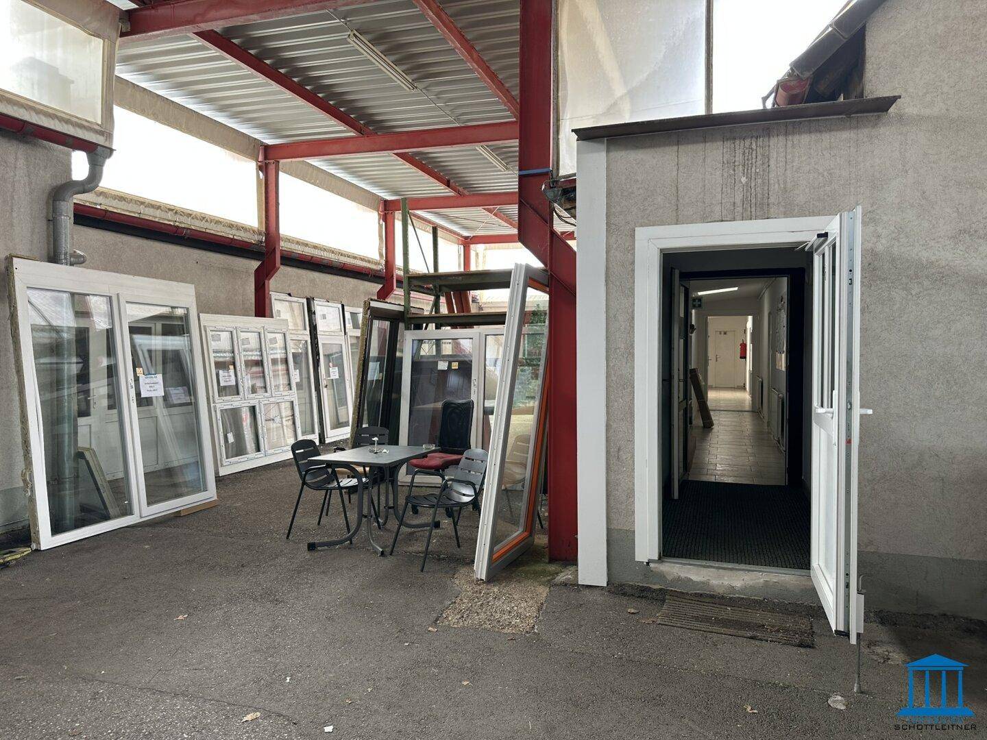 Überdachter Außenbereich mit ausgestellten Fenstern und Türen, sowie einem kleinen Tisch mit Stühlen.