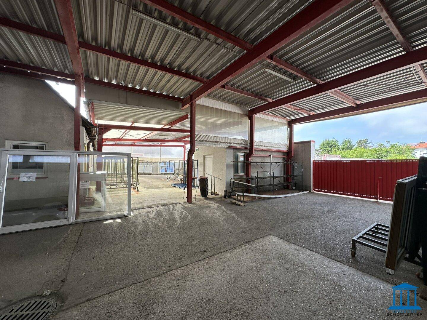 Großer überdachter Außenbereich mit roter Stahlkonstruktion und Blick auf das Gelände.
