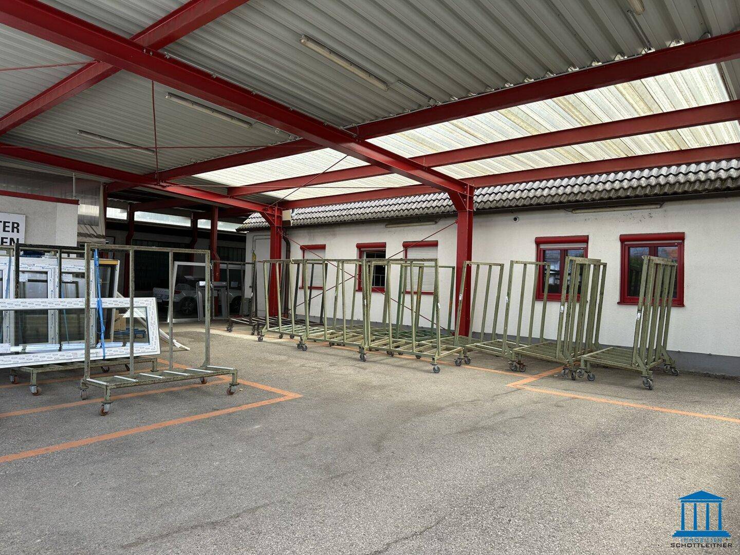 Überdachter Bereich mit roter Stahlkonstruktion und vielen Fensterrahmen zur Lagerung.