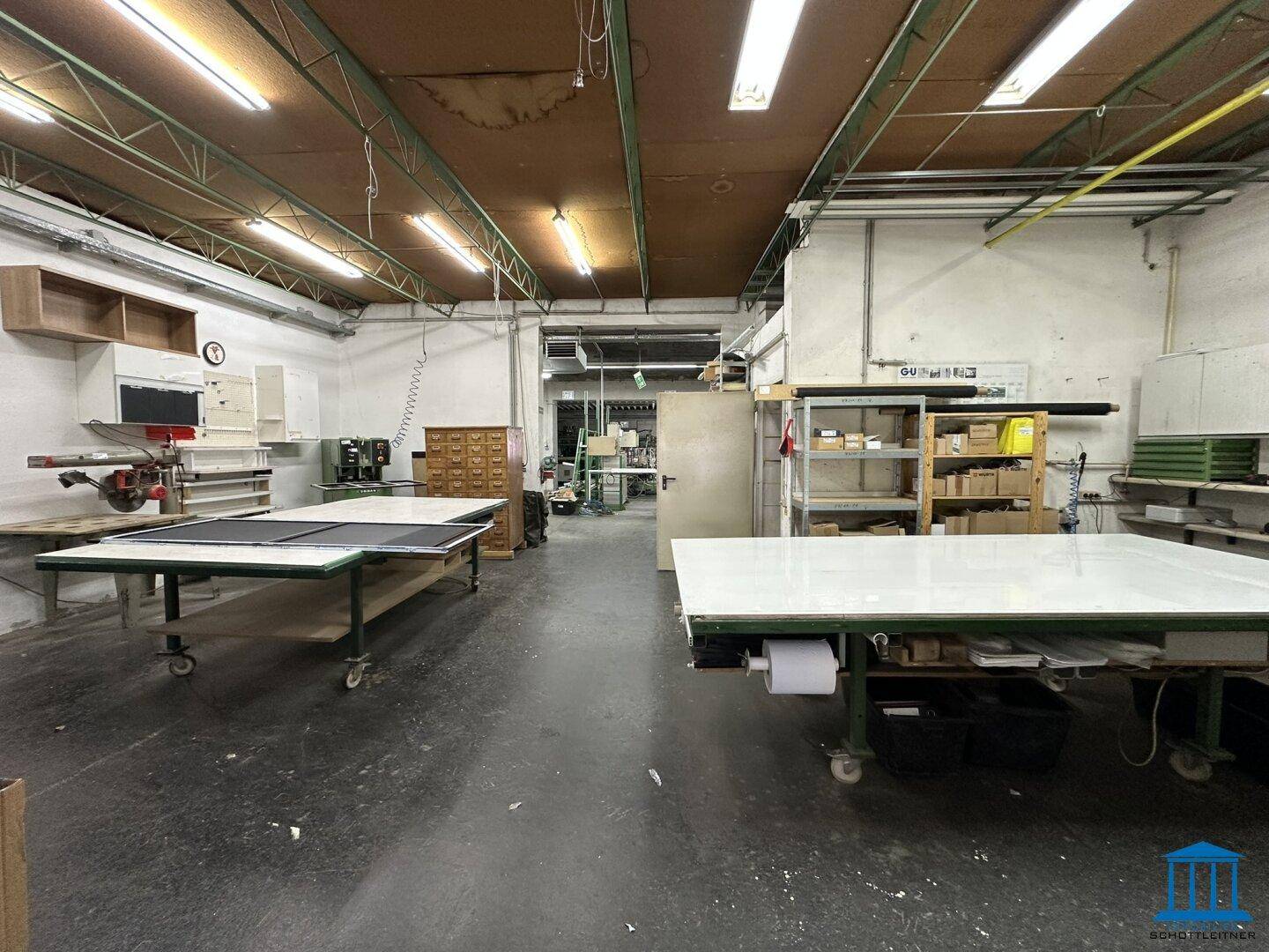 Geräumige Werkstatt mit mehreren Arbeitstischen und Maschinen für handwerkliche Tätigkeiten.