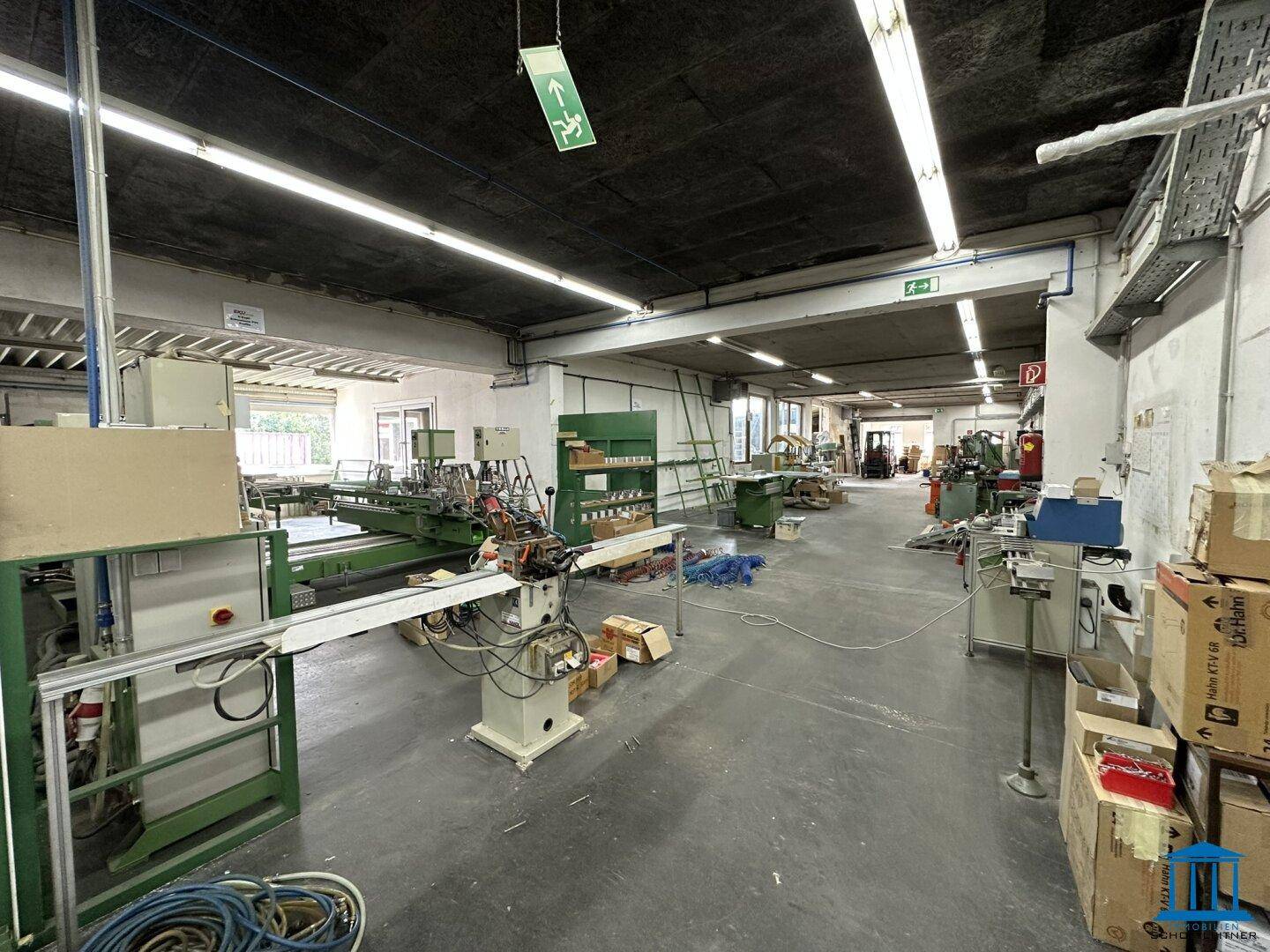Industrielle Werkstatt mit Maschinen, Arbeitstischen und einem Blick auf das Außengelände.