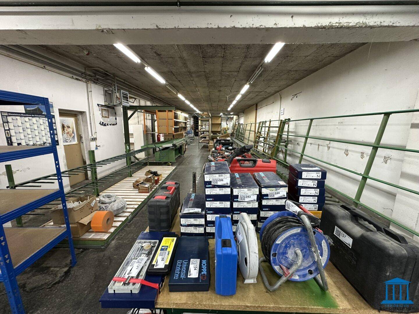 Langer Werkstattbereich mit Werkzeugen, Materialboxen und Regalen, gut beleuchtet durch Deckenleuchten.