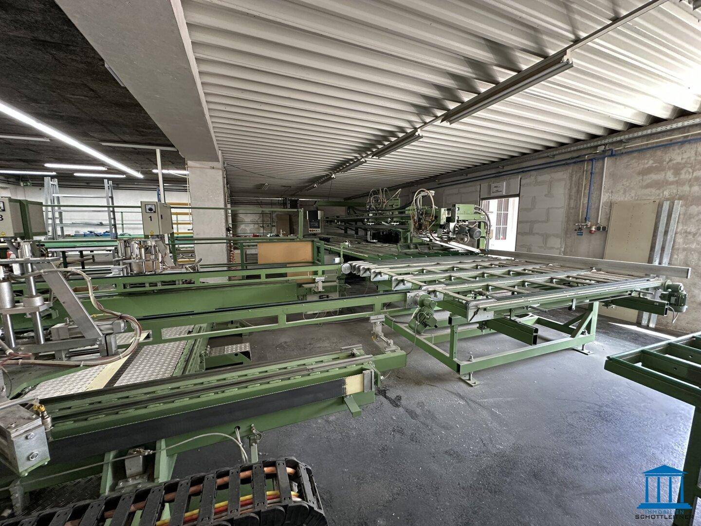 Großer Werkstattraum mit umfangreichen industriellen Maschinen und Förderanlagen unter einem Wellblechdach.