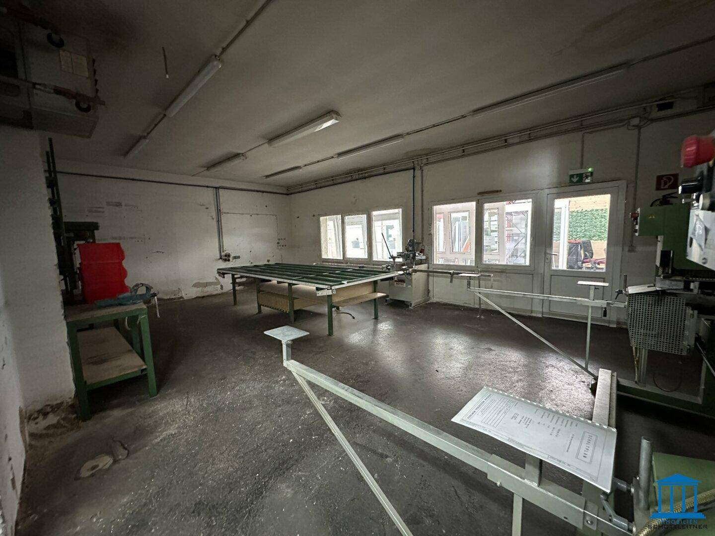 Werkstattbereich mit mehreren Fenstern, einer großen Arbeitsfläche und einigen Maschinen.