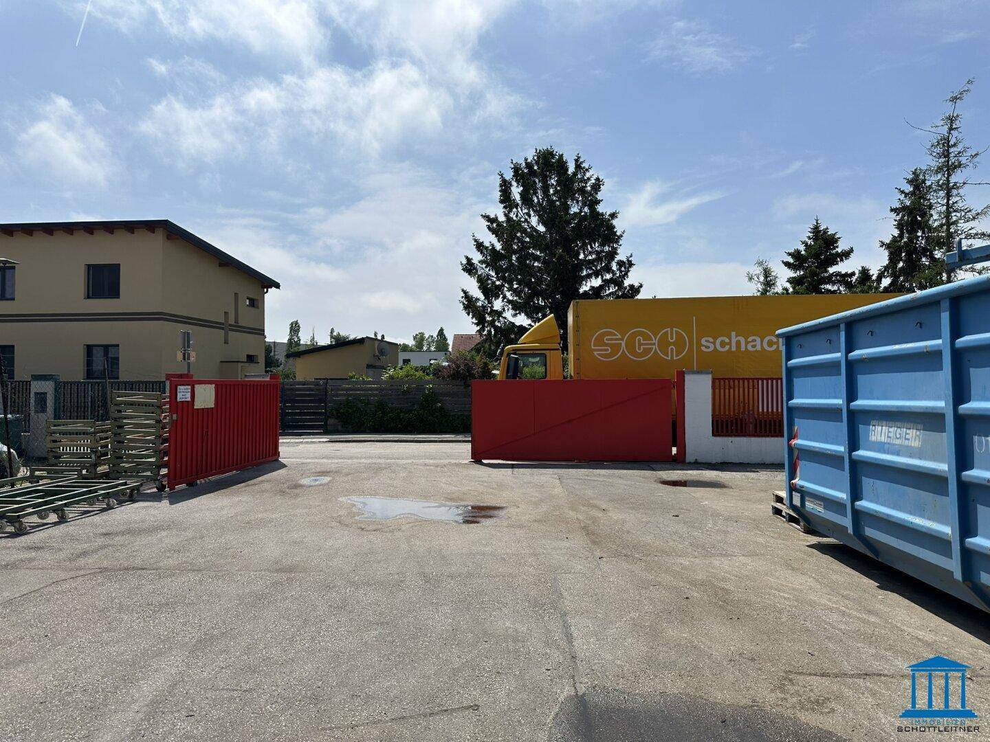 Weitere Außenansicht des Grundstücks mit gepflastertem Bereich, Lastwagen und einem großen blauen Container.