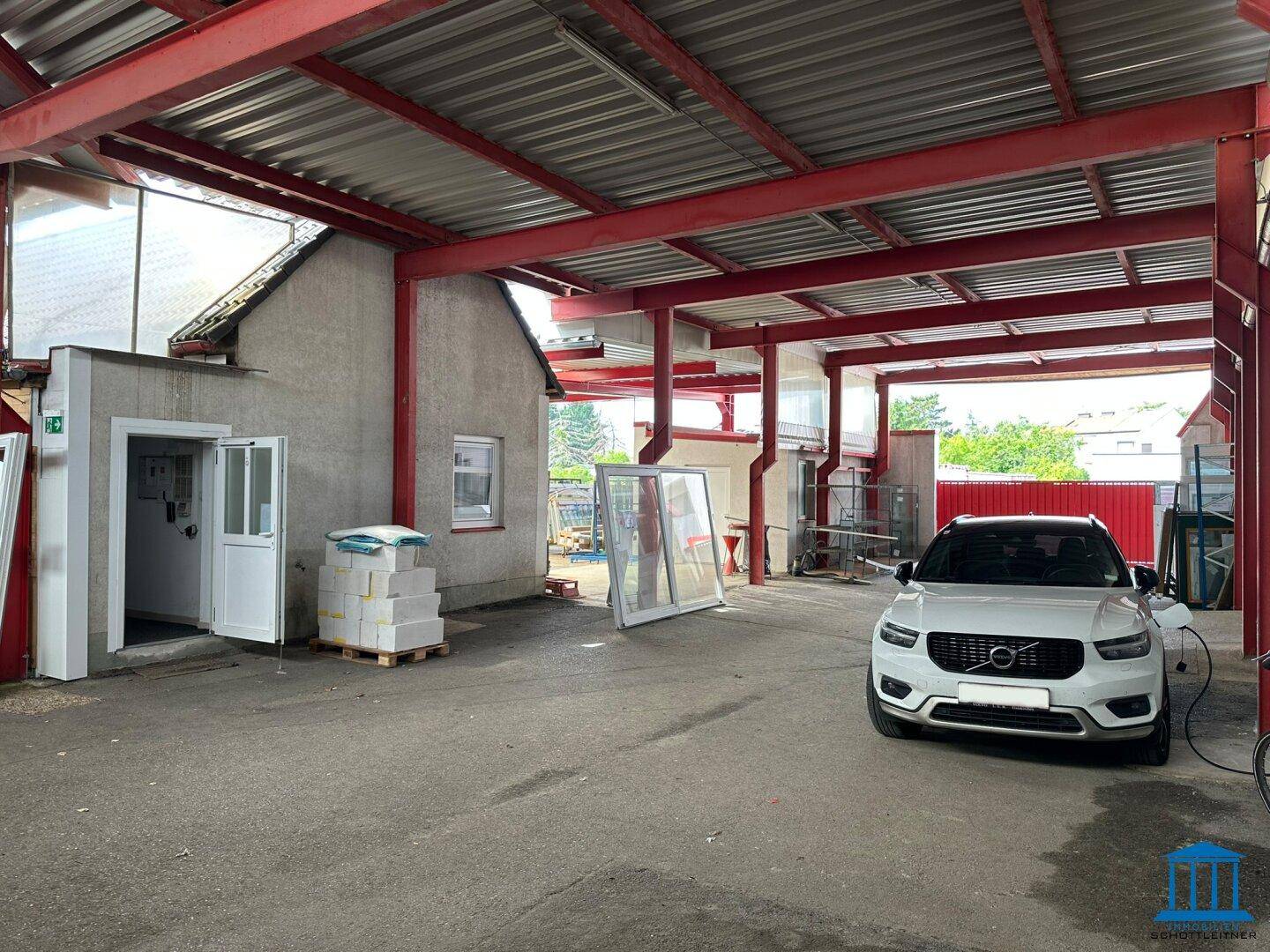 Überdachter Parkplatz mit einem Elektrofahrzeug und einem angrenzenden Gebäude.