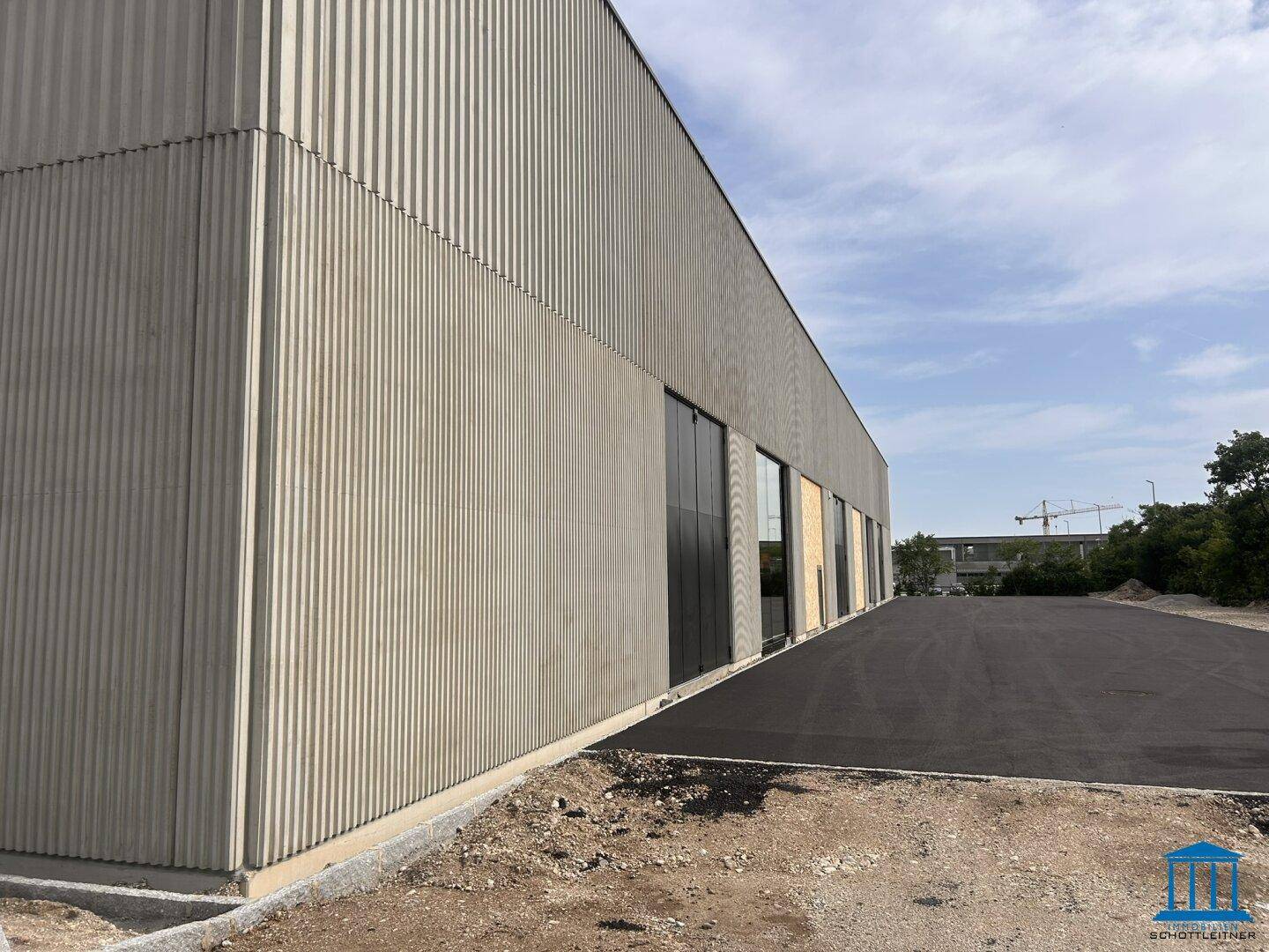 Seitenansicht einer modernen Gewerbeimmobilie mit geriffelter Fassade und asphaltierter Zufahrt.