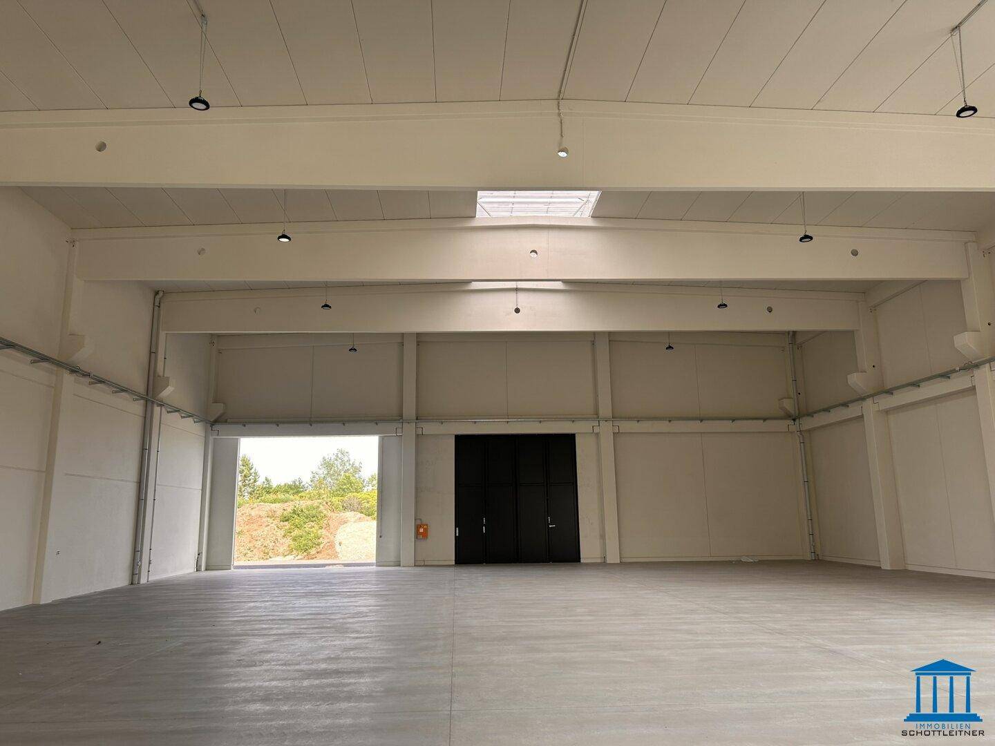 Helle Lagerhalle mit Oberlichtern, hohen Decken und einer großen schwarzen Falttür.