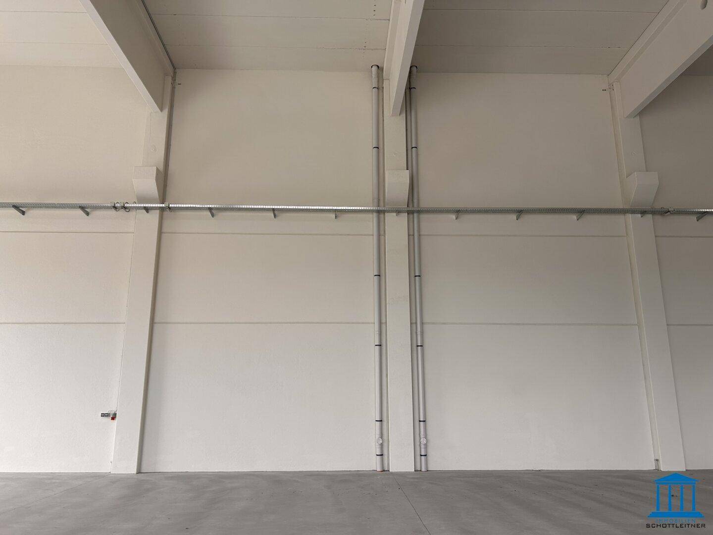 Weiße Wand in einer Halle mit sichtbaren Leitungen und Installationen.