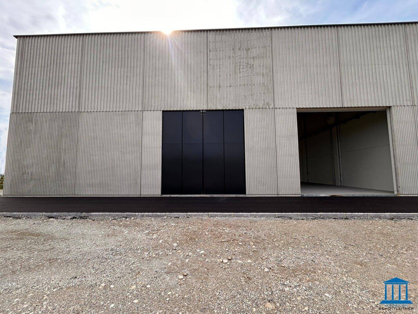Moderne Fassade einer Lagerhalle mit großer schwarzer Falttür und asphaltiertem Vorplatz.