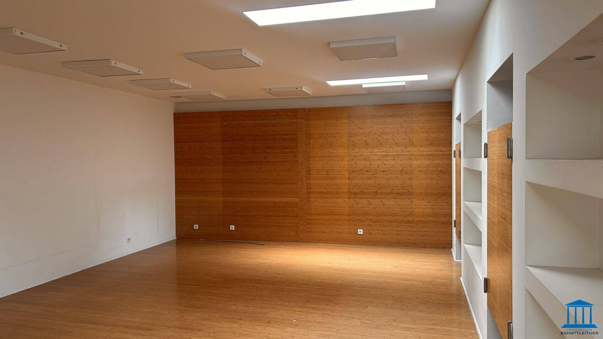 Großer, heller Raum mit Holzfußboden und einer auffälligen Holzakzentwand, ideal für Präsentationen.