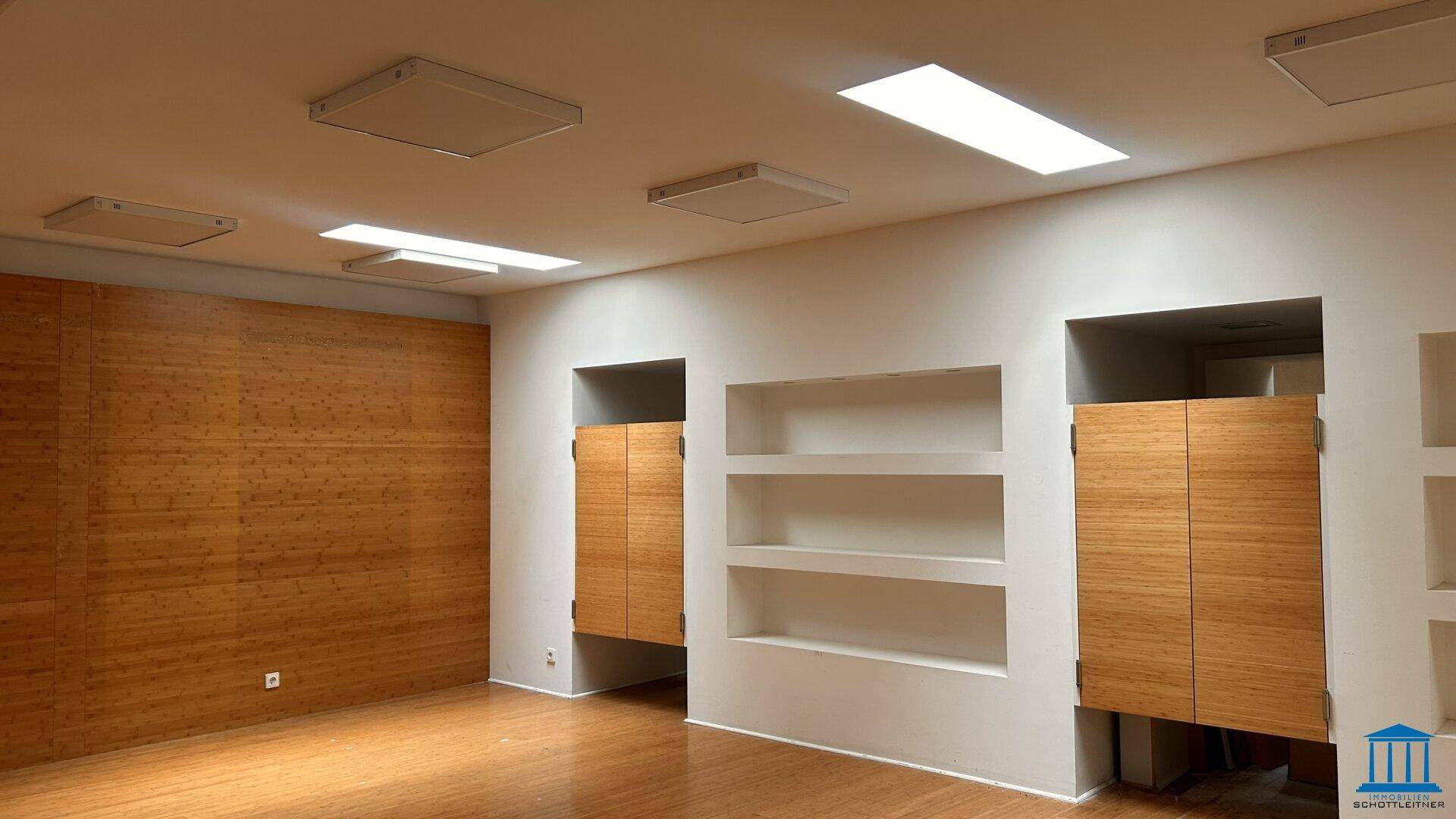 Raum mit Holzakzentwand, Holzfußboden und integrierten Nischen mit Holzfronten für Ausstellungen.